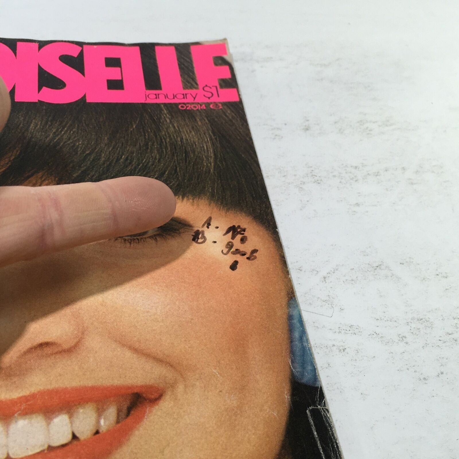 Close-up of the cover of VTG Mademoiselle Magazine: January 1976 revealing handwritten notes next to the model's eye, highlighting vintage decorative style.