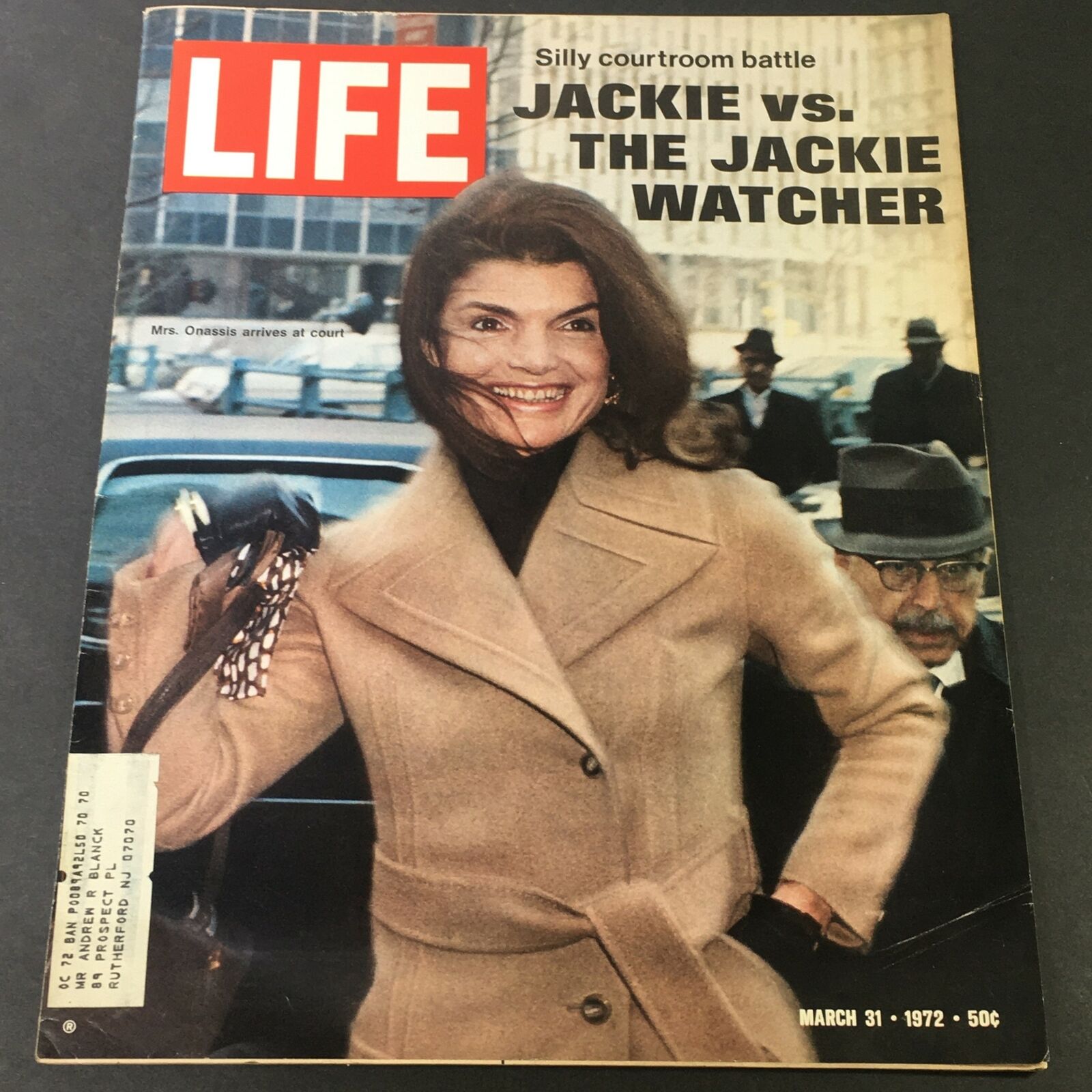 Cover of VTG Life Magazine March 31 1972 featuring an article about Mrs. Jackie Kennedy Onassis and Jackie Watcher, showcasing a stylish woman in a beige coat with a bemused smile, depicting a courtroom theme.