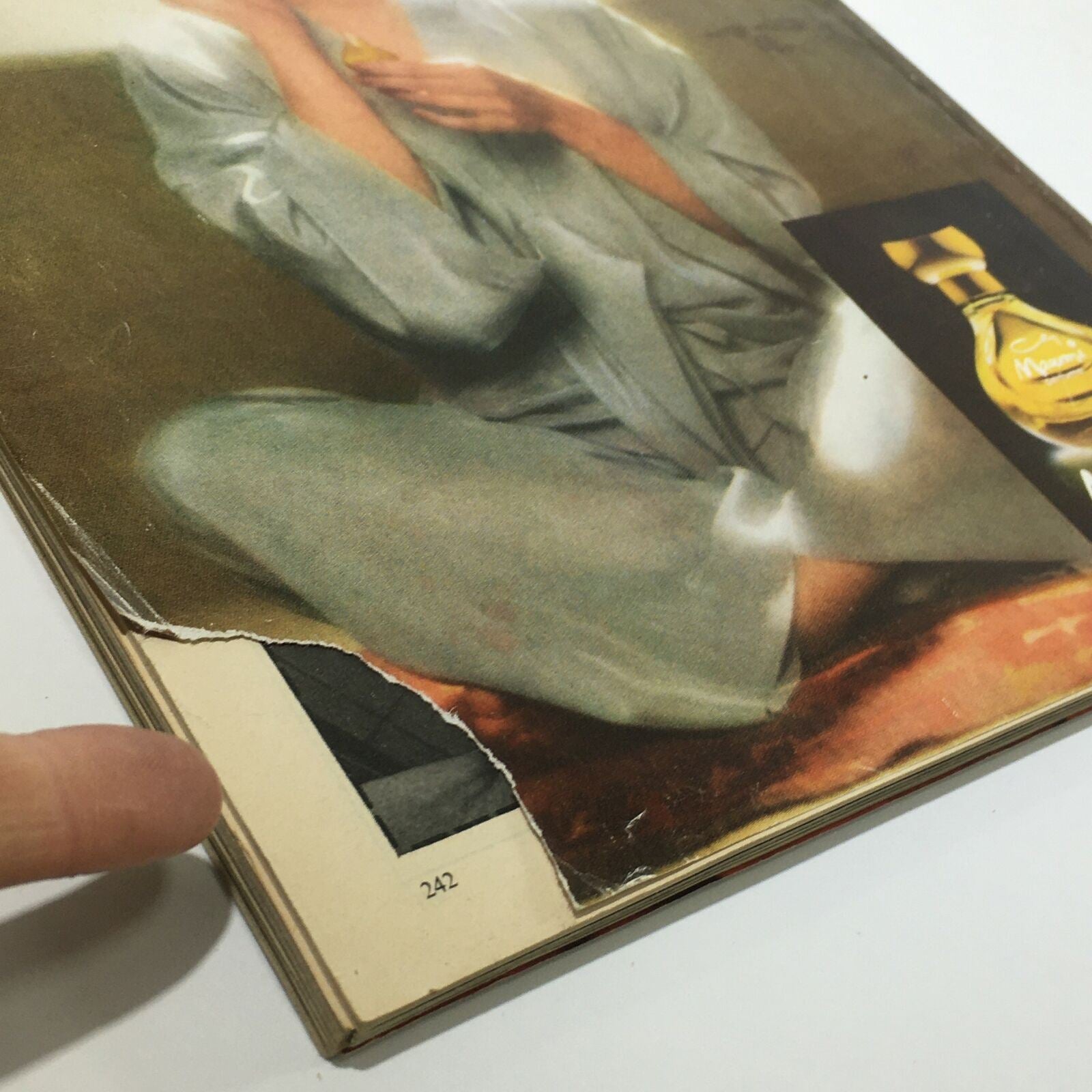 Close-up view of the damaged edge of the Mademoiselle Magazine from November 1976, featuring a beautiful fashion model on the cover. The image shows the tear on the page, highlighting the vintage condition of this collectible magazine.