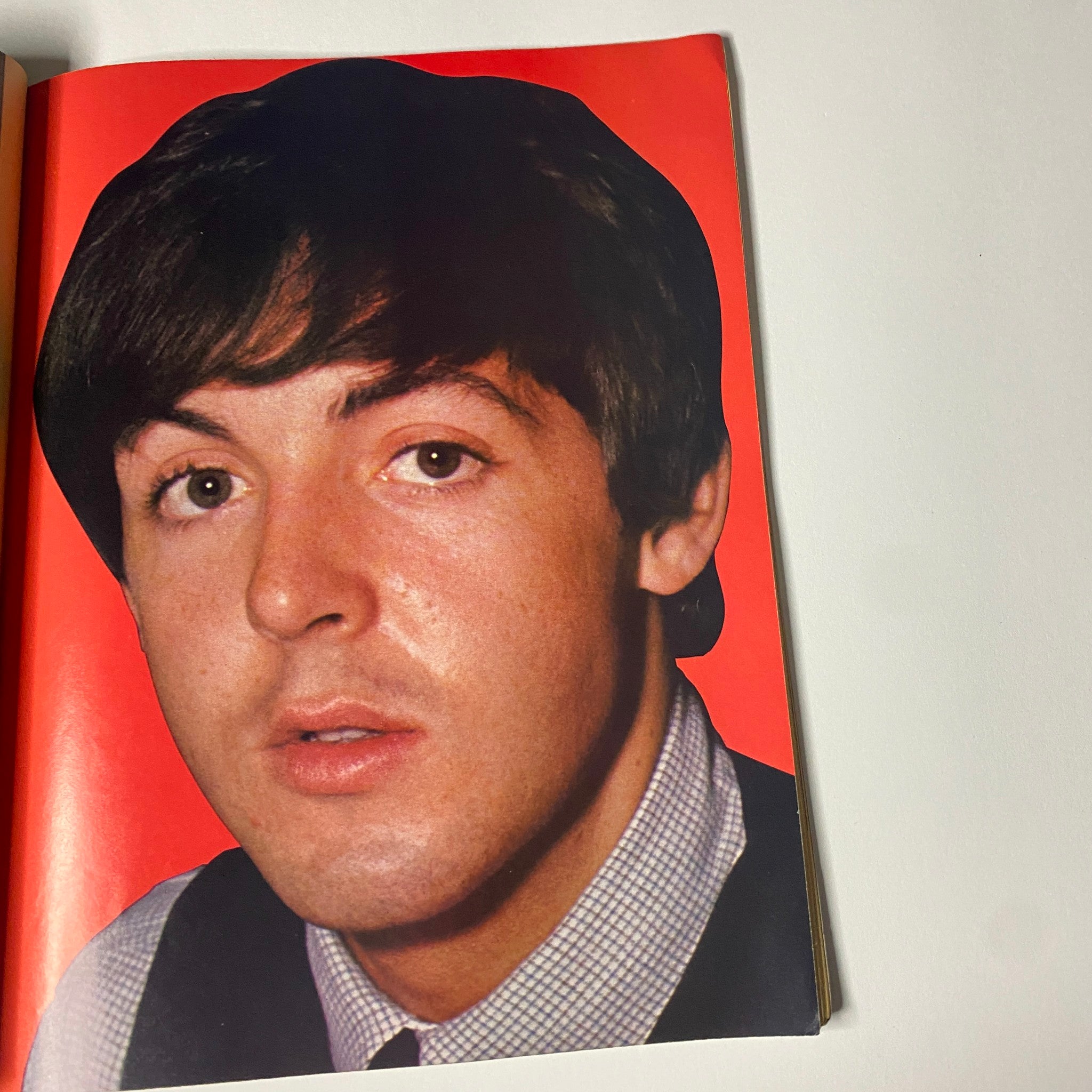 Photo of Paul McCartney from the '1966 16 Scoop: The Beatles Whole True Story' magazine, capturing a close-up of the iconic musician with a vibrant red background.
