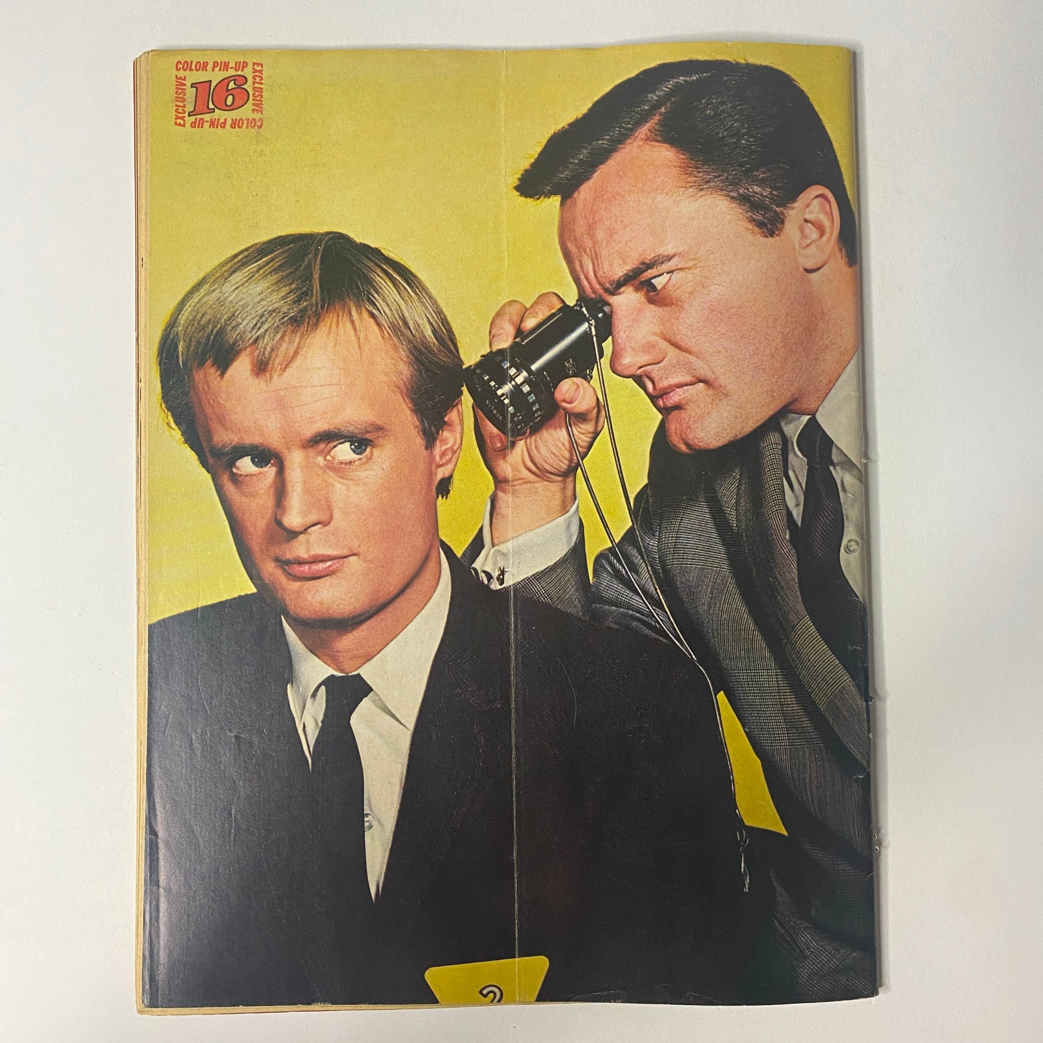 Cover of 16 Magazine December 1966 Vol 8 No. 7 featuring The Beatles with a unique color pin-up. Illustrated image of two male figures, one peering through a camera at the other, reflecting the pop culture of the 1960s.