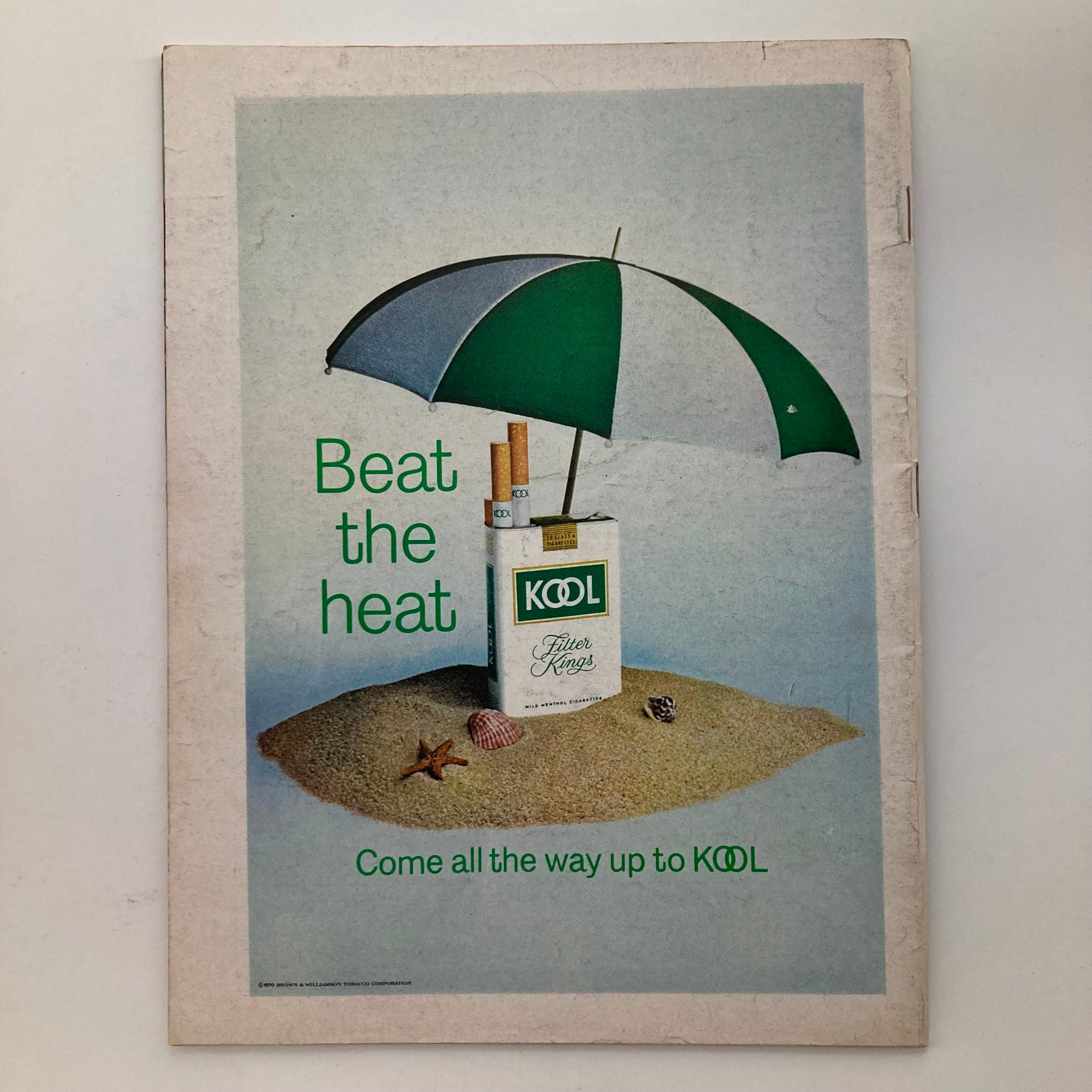 Vintage advertisement from VTG Newsweek Magazine August 10, 1970, featuring a pack of KOOL cigarettes under a green beach umbrella, promoting the theme 'Beat the Heat' on a sandy background.