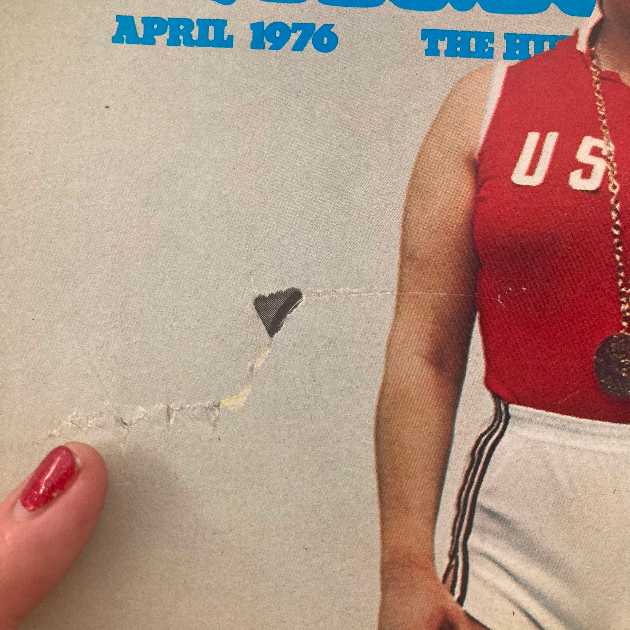 Close-up of the front cover of the Vintage National Lampoon Magazine from April 1976, featuring a damaged corner and a U.S. athlete wearing a medal.