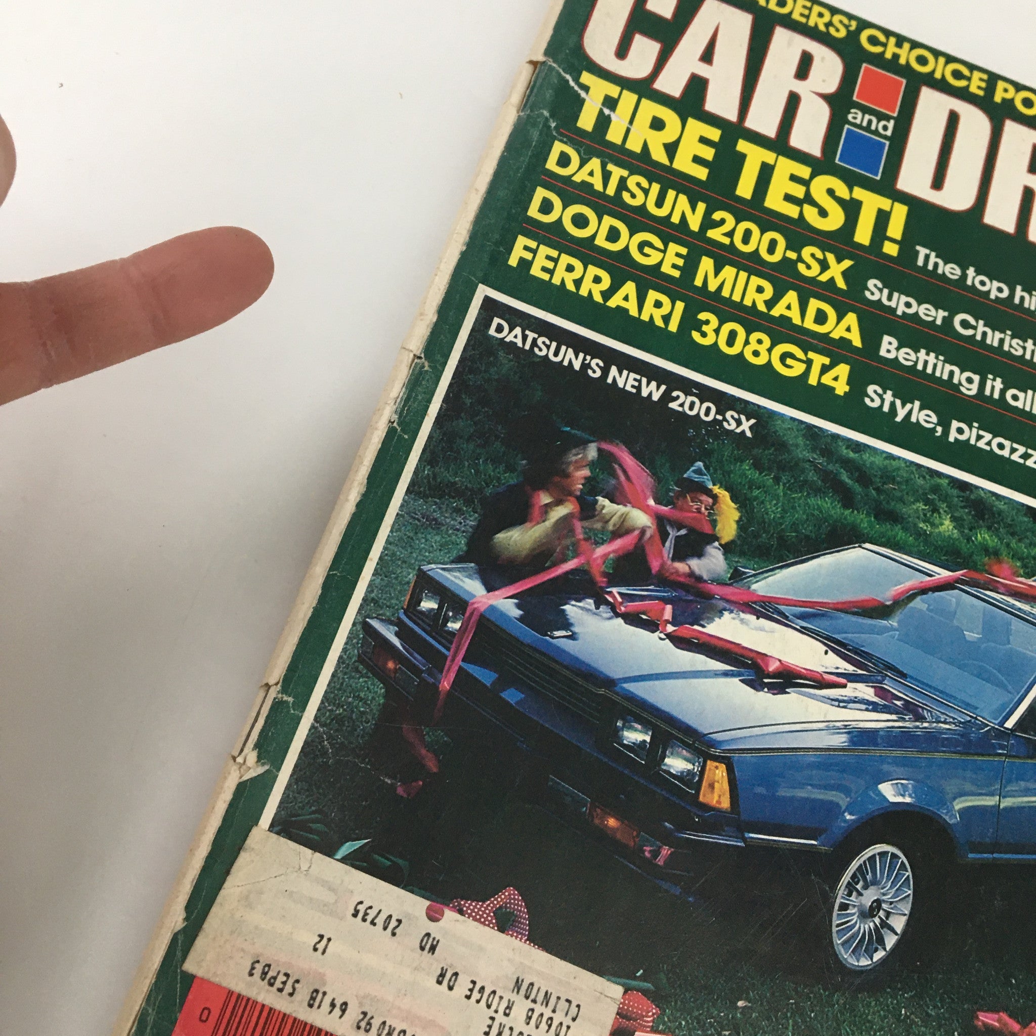 Detailed view of the VTG Car and Driver Magazine December 1979 cover with 'Swarming Over New Datsun 200-SX Coupe'. The image displays the magazine title and vibrant graphics along with a Datsun 200-SX adorned with ribbons. A finger pointing towards the title is visible.