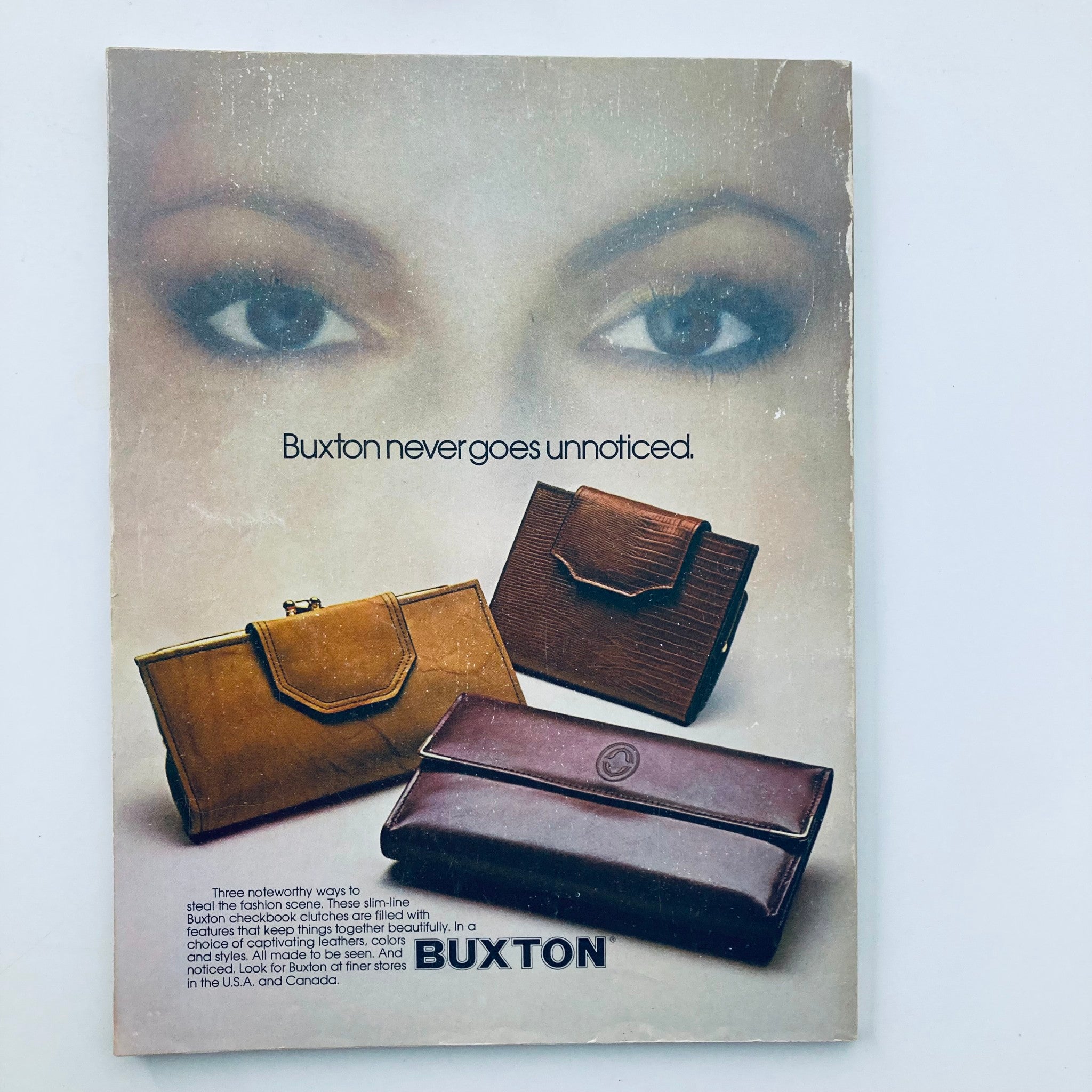 Promotional image for Buxton leather accessories featuring three handbags: a brown clutch, a textured brown bag, and a sleek dark brown wallet. Text reads 'Buxton never goes unnoticed.' This image is from the VTG Seventeen Magazine December 1979 Olympic Games Keepsakes.