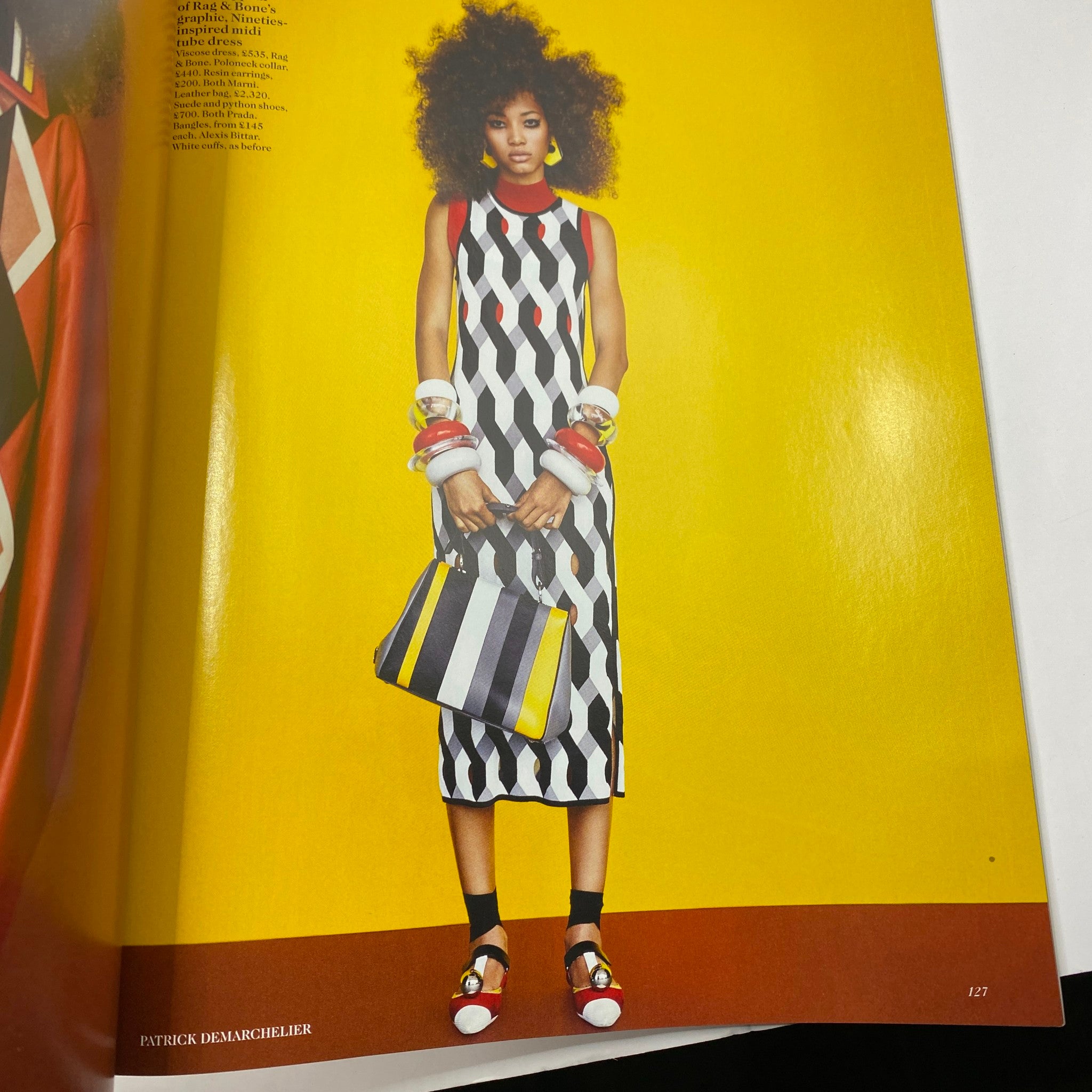 Fashion editorial from British Vogue UK Magazine February 2016, displaying a model in a colorful, graphic dress against a vibrant yellow background.