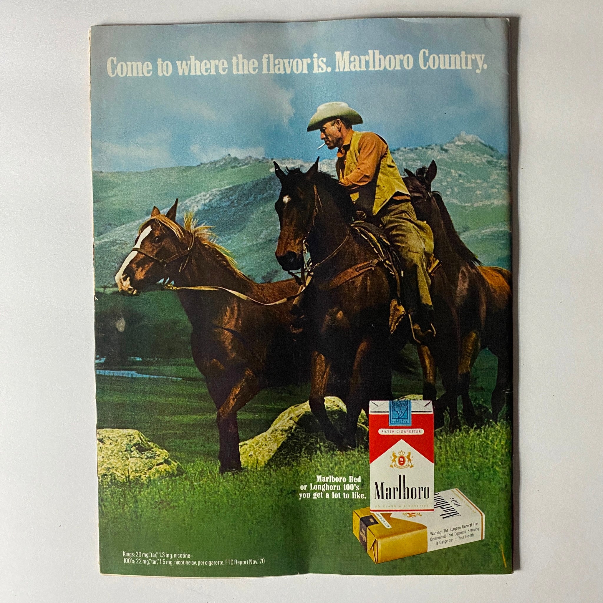 Vintage advertisement for Marlboro cigarettes, depicting a cowboy on horseback in a scenic landscape, accompanied by the slogan 'Come to where the flavor is. Marlboro Country'.