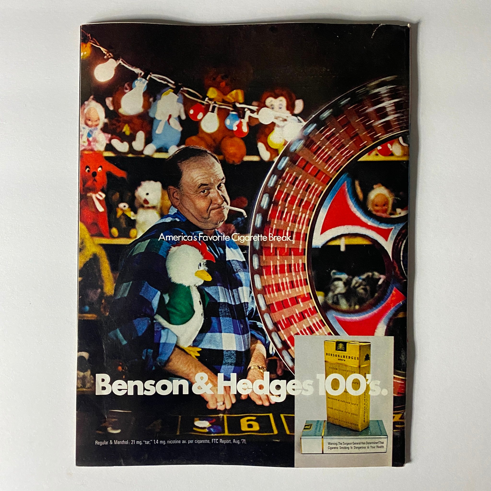 Vintage advertisement for Benson & Hedges cigarettes, showcasing a man in a plaid shirt with a toy duck, set against a colorful carnival background.