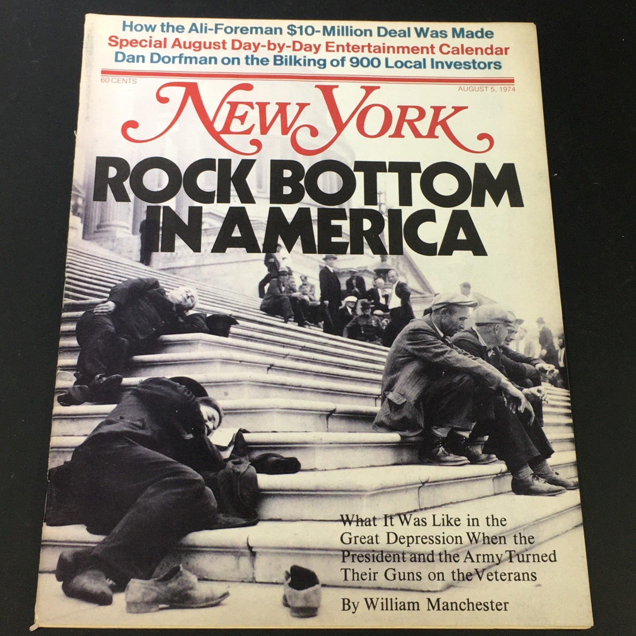 Cover of the VTG New York Magazine dated August 5, 1974, featuring the title 'Rock Bottom in America'. The cover displays a dramatic black and white photograph depicting individuals resting on the steps amidst crowds, reflecting the economic struggles of the 1970s. The issue offers insights into American societal issues during this pivotal time in history.