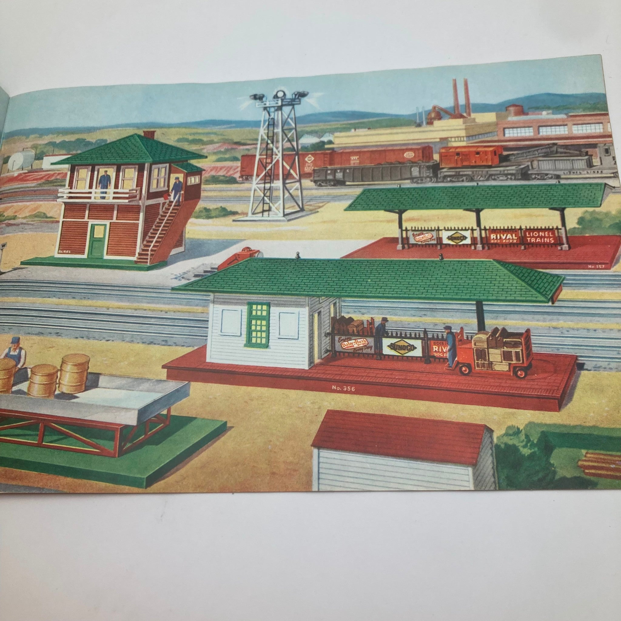 Illustration from the 1952 Lionel Model Railroad Train Scout 3-Car Freight Catalog depicting a train station and industrial setting with various buildings.