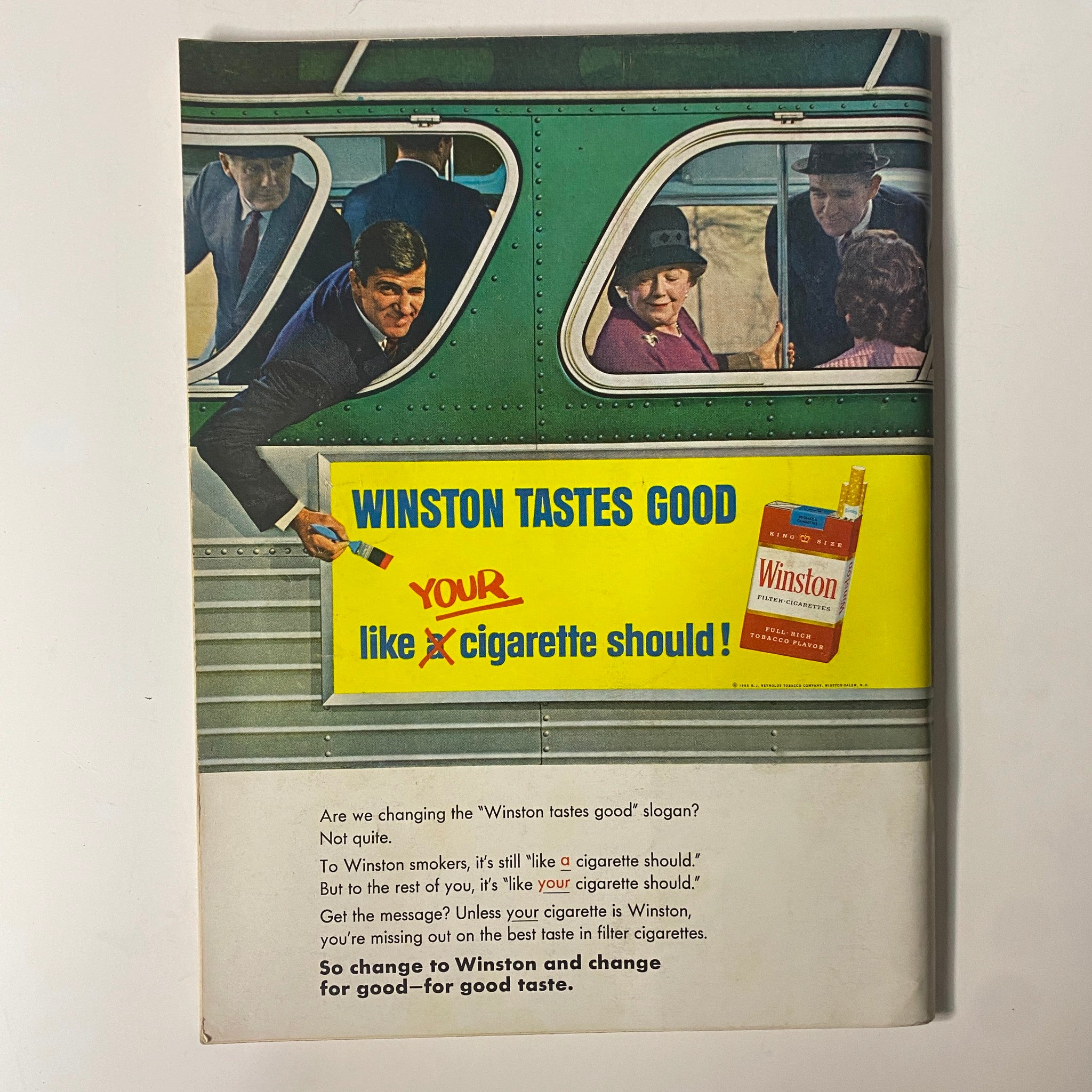 Advertisement featuring a vintage Winston cigarette ad from Playboy Magazine August 1966. The image showcases a man outside a bus holding a brush, interacting with a vibrant sign that reads 'WINSTON TASTES GOOD like your cigarette should!' while passengers look on. This ad reflects the advertising style of the 1960s era. Relevant to Playboy Magazine August 1966 featuring Susan Denberg as Playmate of the Month.