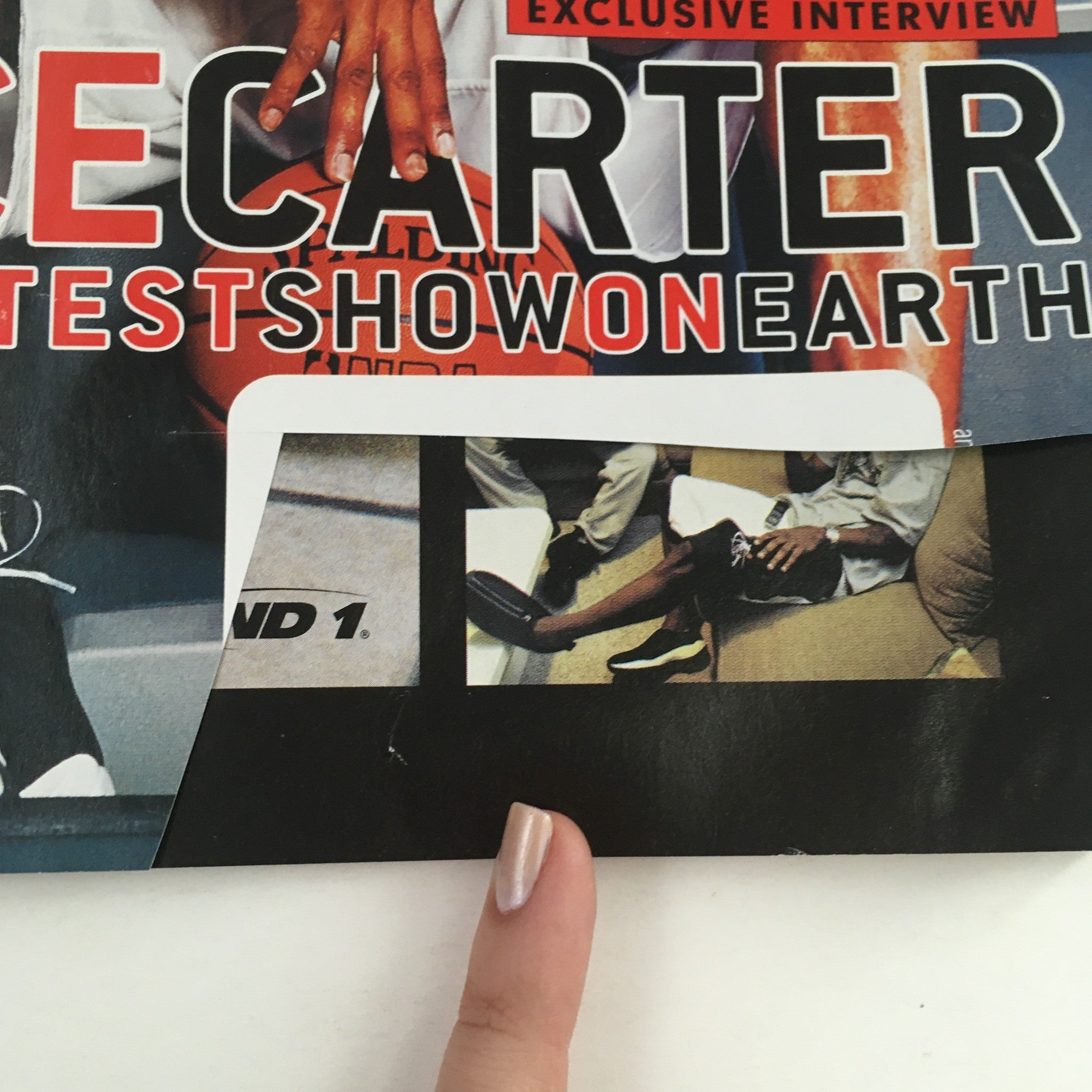 Close-up image of the Slam Magazine April 2000 cover featuring Vince Carter with a partial view of a finger pointing to the magazine text. The cover promotes an exclusive interview and showcases notable basketball themes.