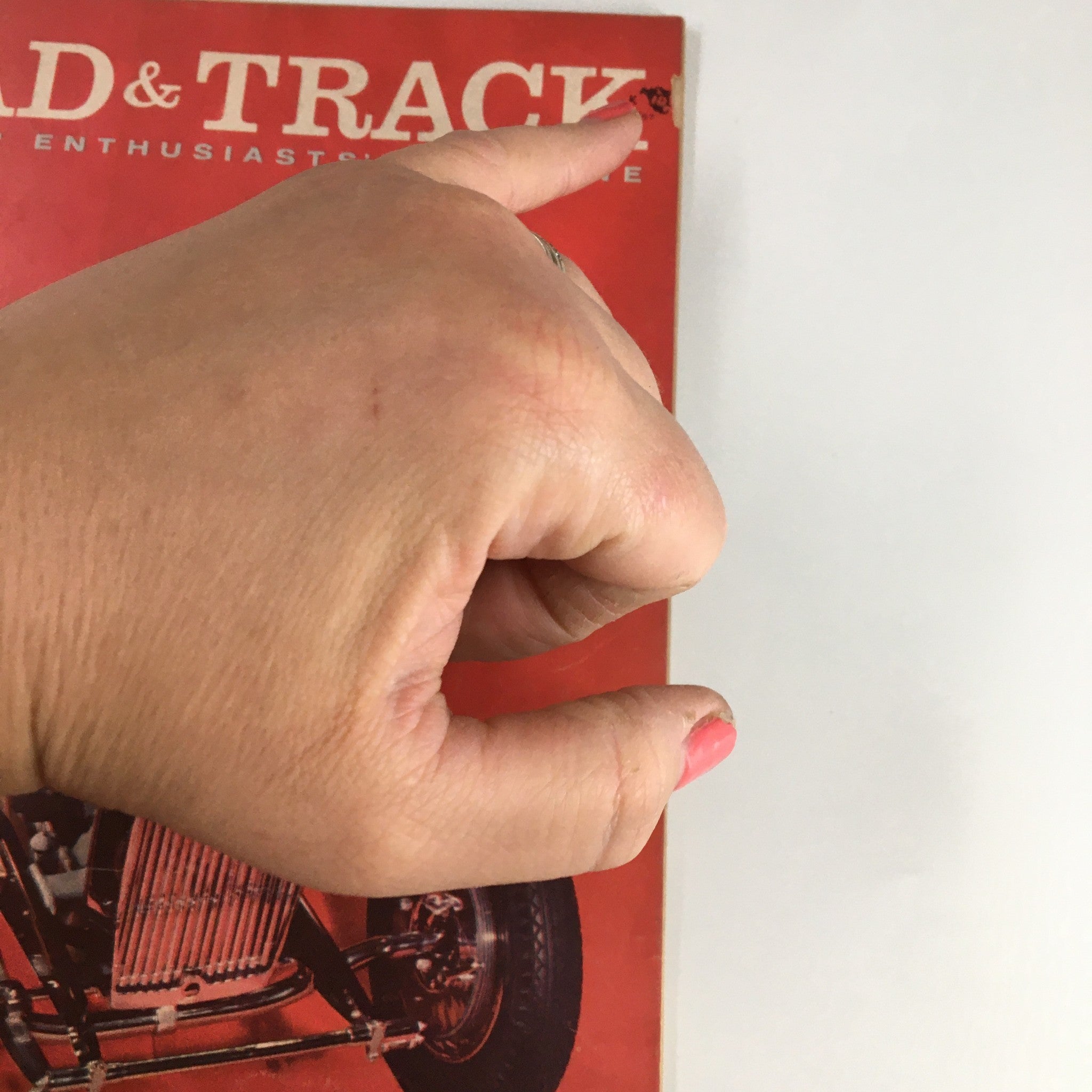 Close-up view of the vintage Road & Track Magazine from October 1957 featuring Mercedes 219 road test, showing hand gesture pointing to the title.