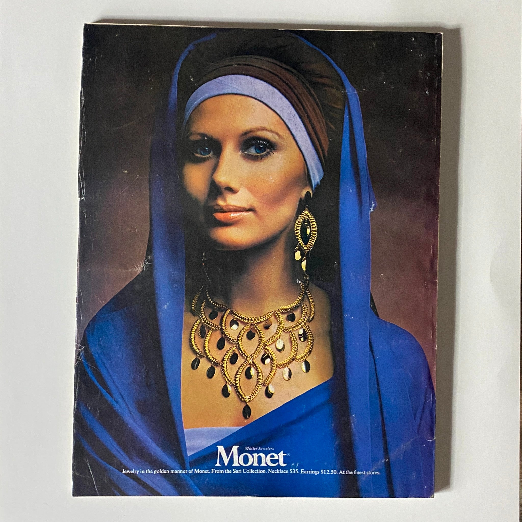 Cover of the jewelry catalog by Monet featured in VTG Vogue Magazine September 15, 1970, displaying a model adorned in elaborate gold jewelry, set against a striking background.