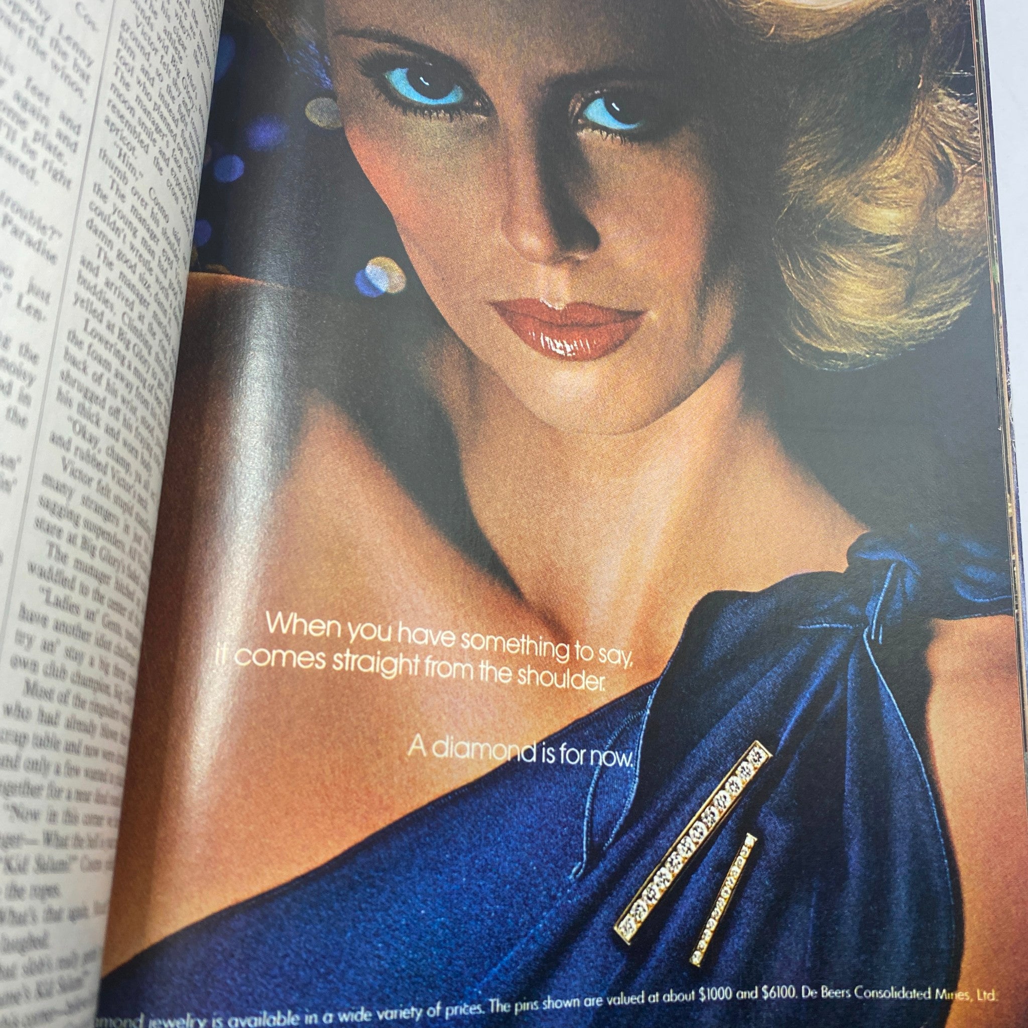 Vintage Vogue Magazine December 1977 advertisement showcasing a glamorous model with striking blue eyes, wearing a blue dress and diamond brooch, emphasizing elegance and style.