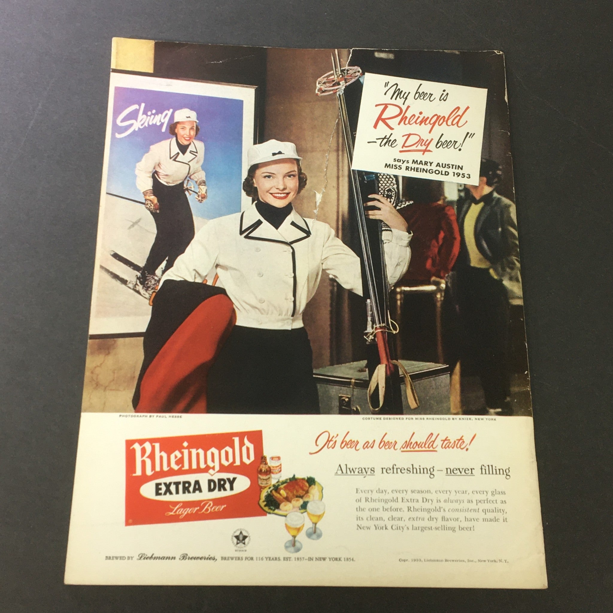Vintage advertisement for Rheingold Extra Dry Lager Beer, featuring Miss Rheingold 1953, showcasing a stylish woman in a ski outfit with colorful background and promotional text.