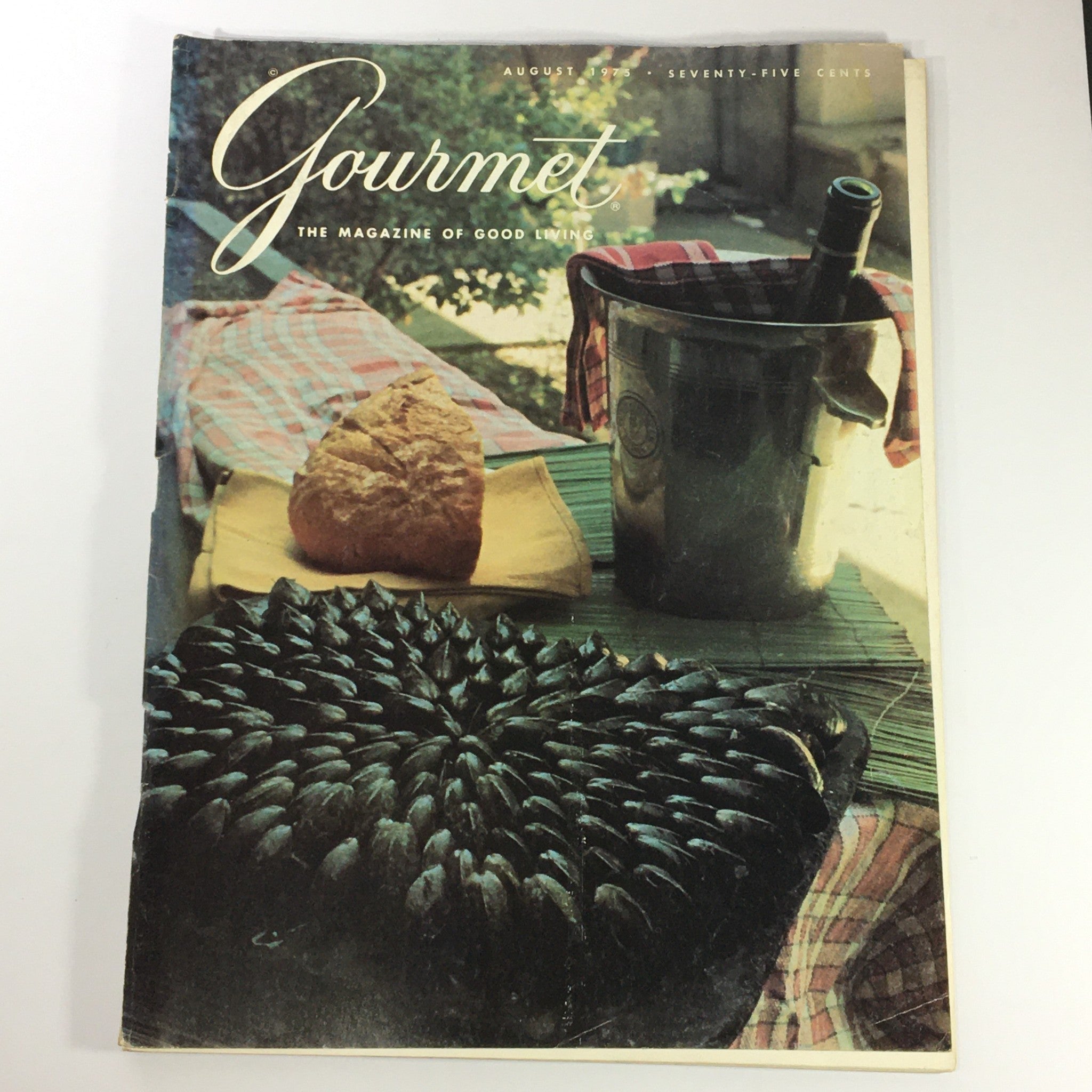Cover of VTG Gourmet The Magazine of Good Living August 1975 showcasing a rustic dining setting with a loaf of bread and a bottle in a cooler.