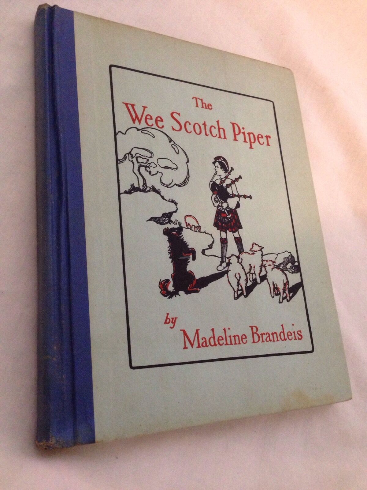 Cover of 'The Wee Scotch Piper Book' by Madeline Brandeis, featuring a Scottish piper surrounded by playful animals, including a dog and sheep, with a scenic background.
