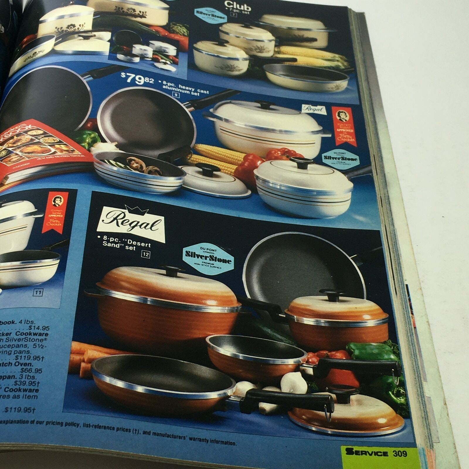 VTG Service Merchandise Catalog Showroom 1983-1984 Volume 14 featuring a display of cookware sets, including an 8-piece heavy cast aluminum set and a Regal 8-piece 'Desert Sand' set, showcasing various pots and pans on a vibrant kitchen layout.