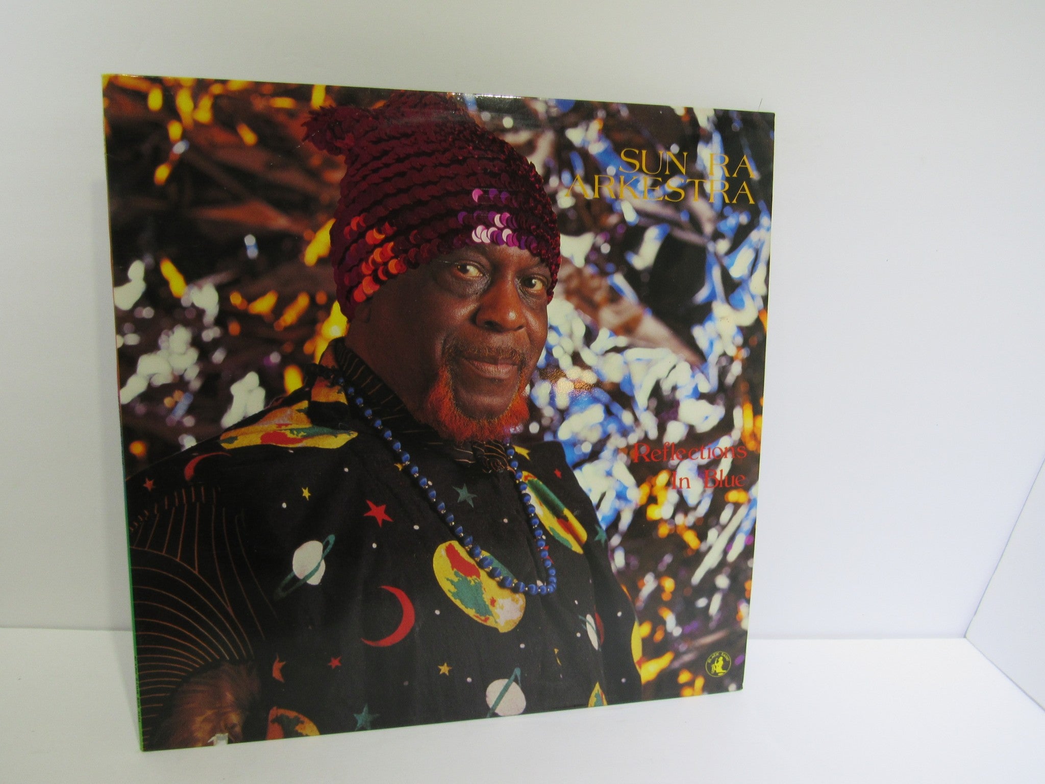 Album cover of 'Sun Ra Arkestra: Reflections In Blue', showcasing Sun Ra in a colorful outfit with a reflective backdrop.