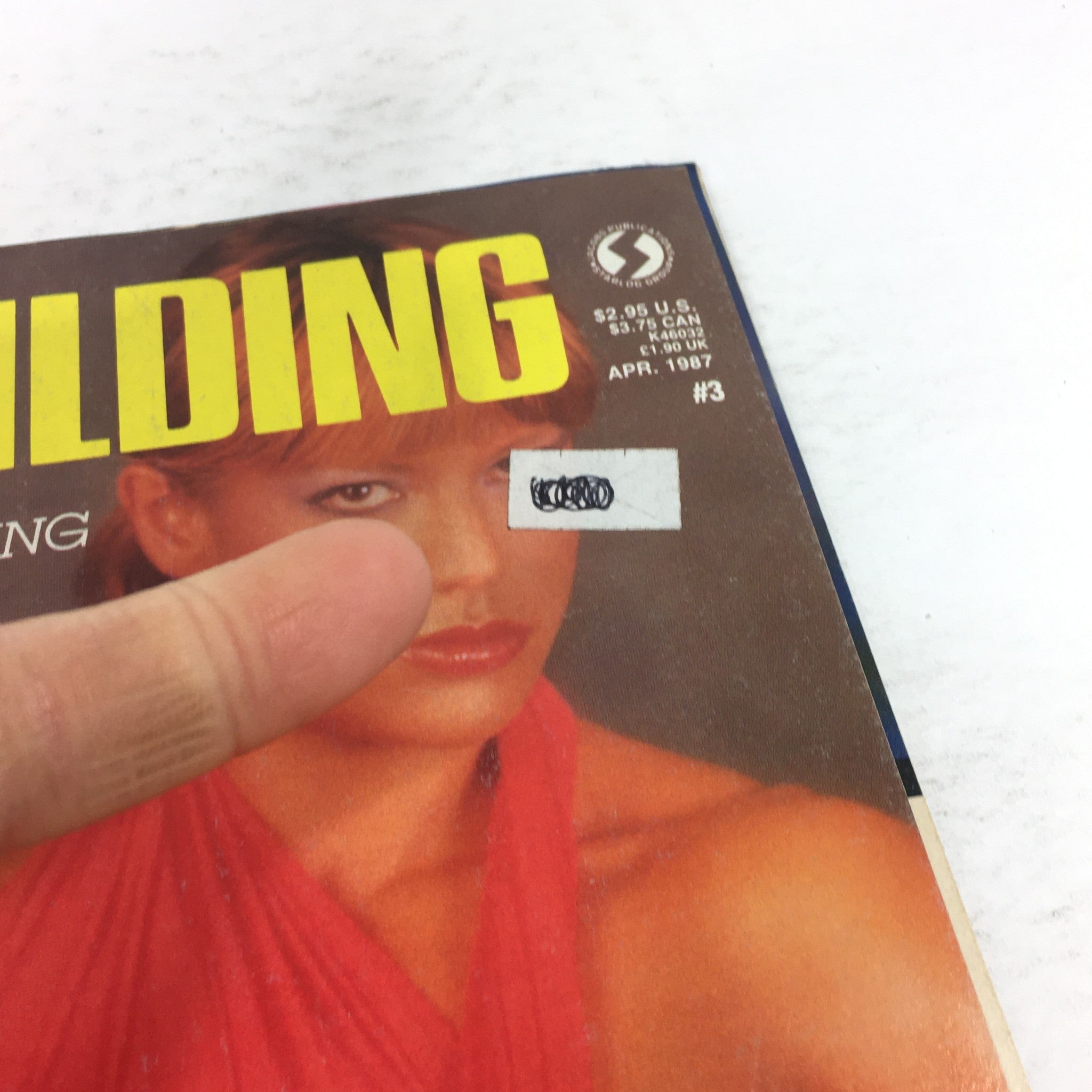 Close-up of the cover of VTG Female Body Building magazine from April 1987, showing the title and a finger pointing at a price sticker, emphasizing the vintage aspect of the publication.