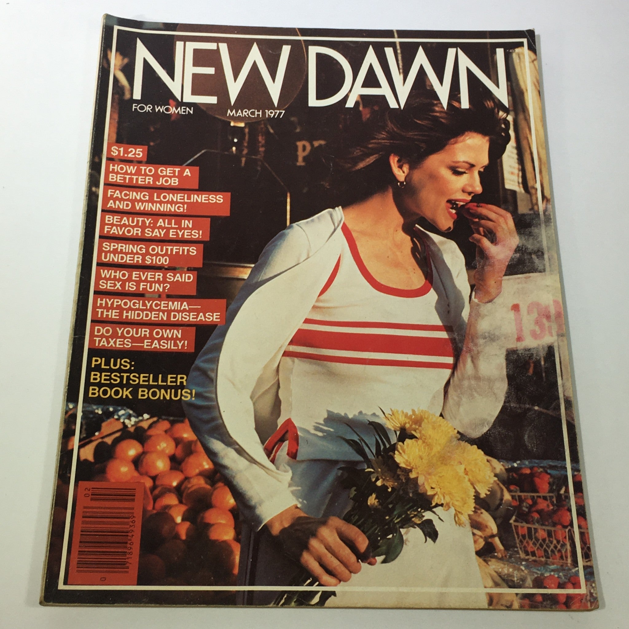 Cover of VTG New Dawn Women's Magazine: March 1977 featuring a woman in a white and red striped outfit holding yellow flowers, surrounded by a market scene. The magazine discusses topics like spring outfits and beauty tips.