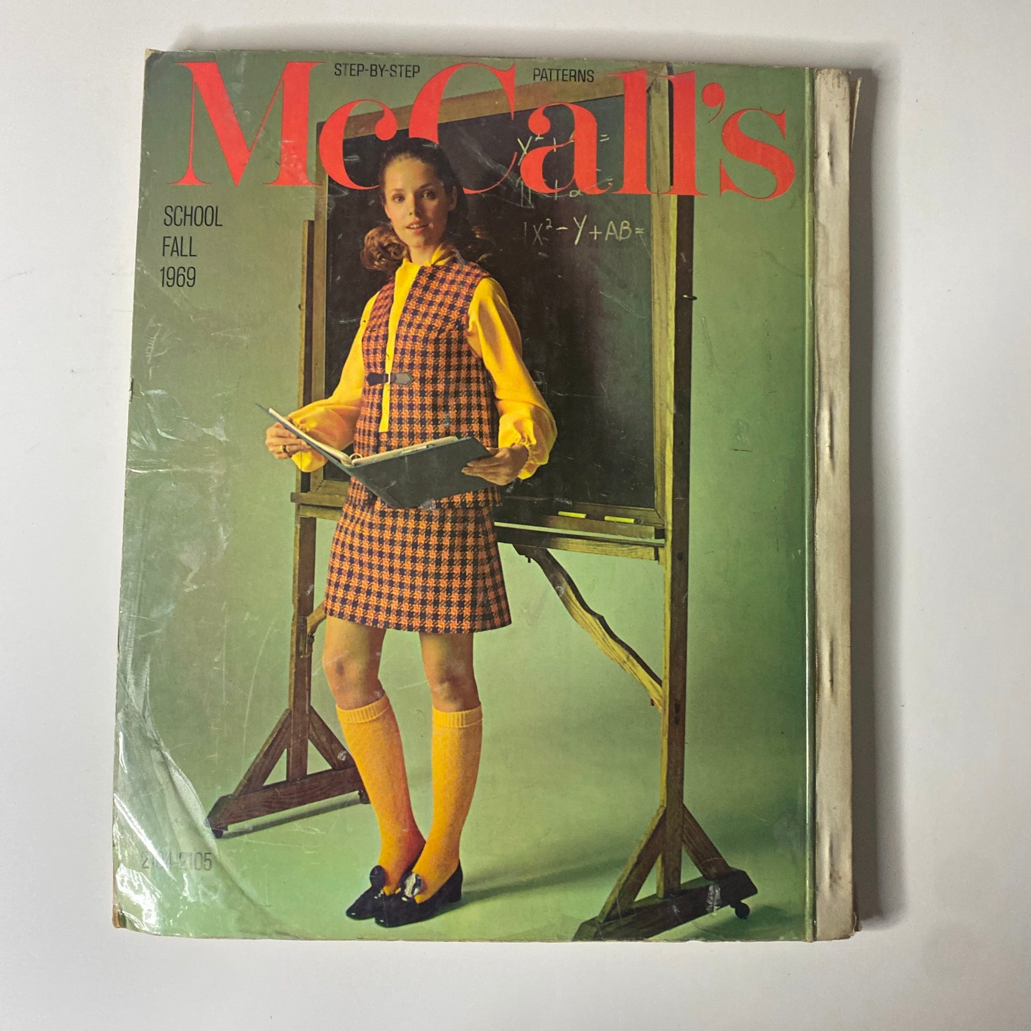 Cover of the 1969 McCall's School Fall catalog featuring a girl in a stylish checkered outfit, holding a book in front of a chalkboard, highlighting fashion sewing patterns for school.