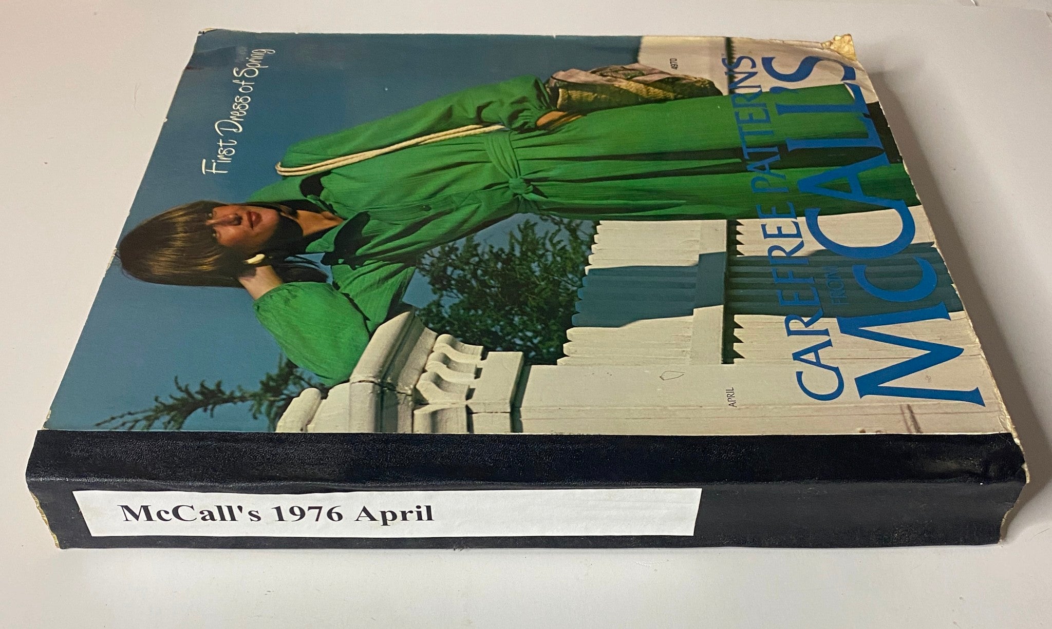 Side view of the 1976 April Carefree Patterns McCall's Spring Catalog showing a model in a green dress, with a white fence in the background.