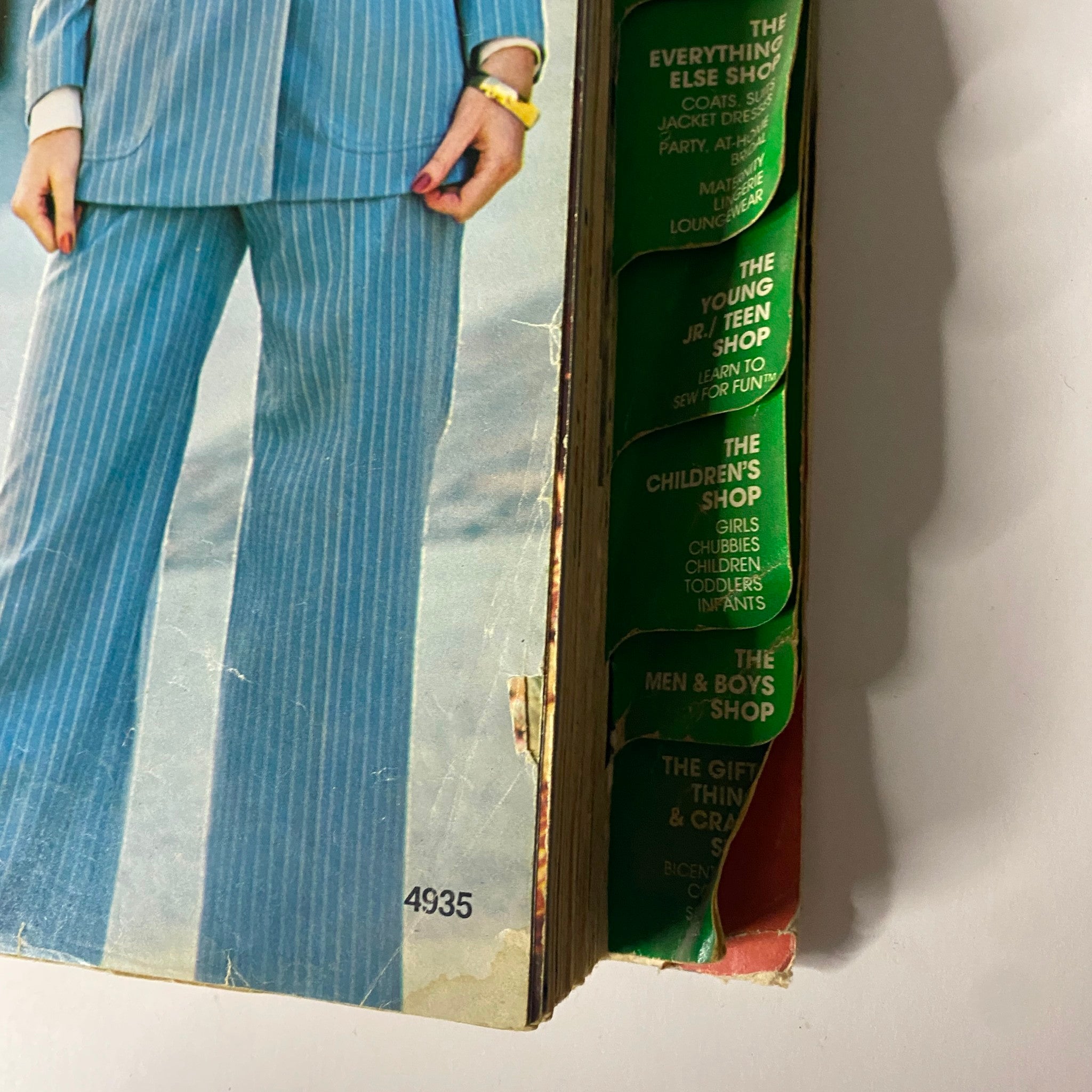 Close-up view of the 1976 April Carefree Patterns McCall's Spring Catalog spine, featuring various shop sections including Men's, Children's, and Teen's fashion.