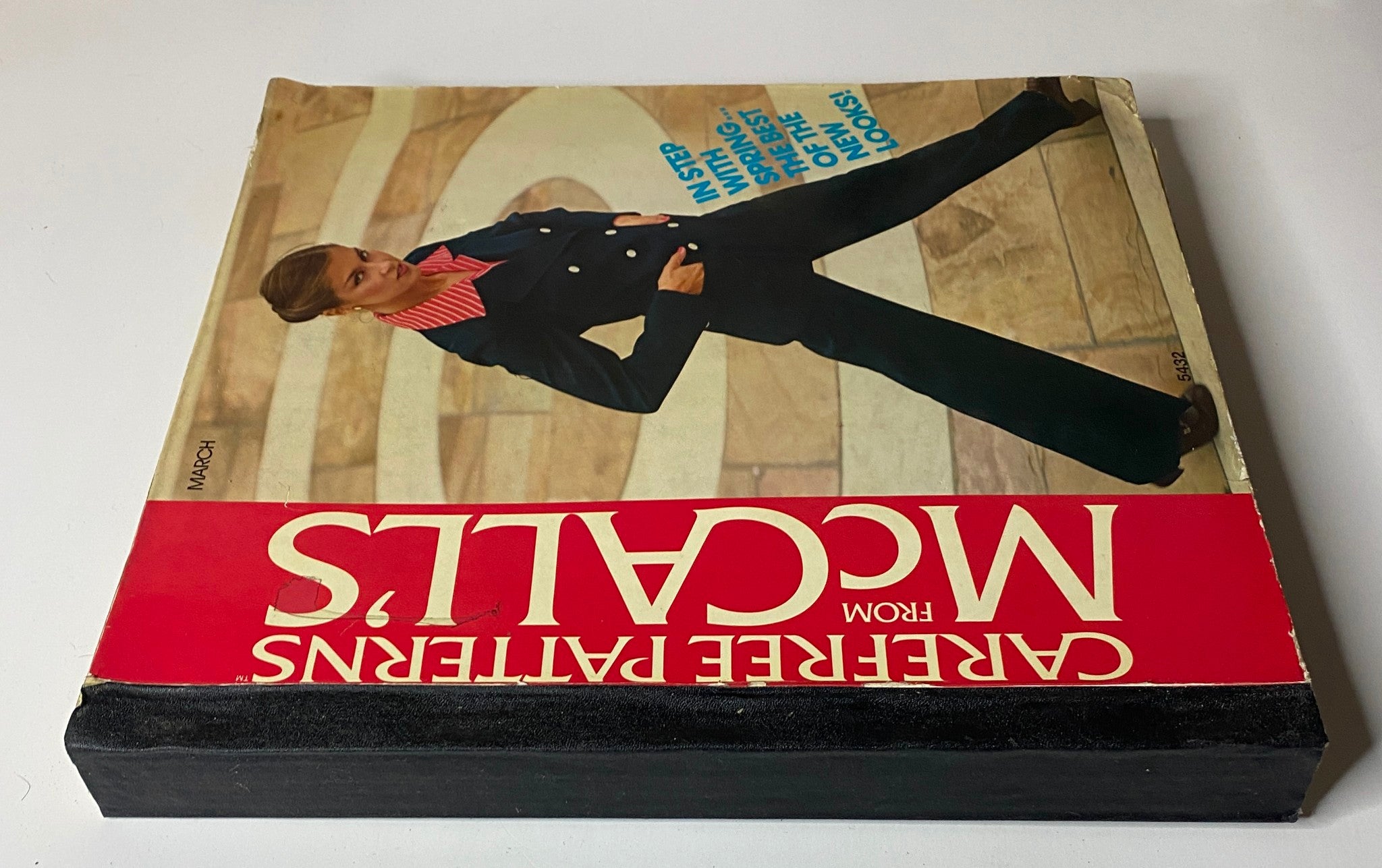Side view of the 1970s March Carefree Patterns from McCall's Catalog, highlighting the cover with a model in a navy suit and pink striped collar, promoting spring wardrobe options.