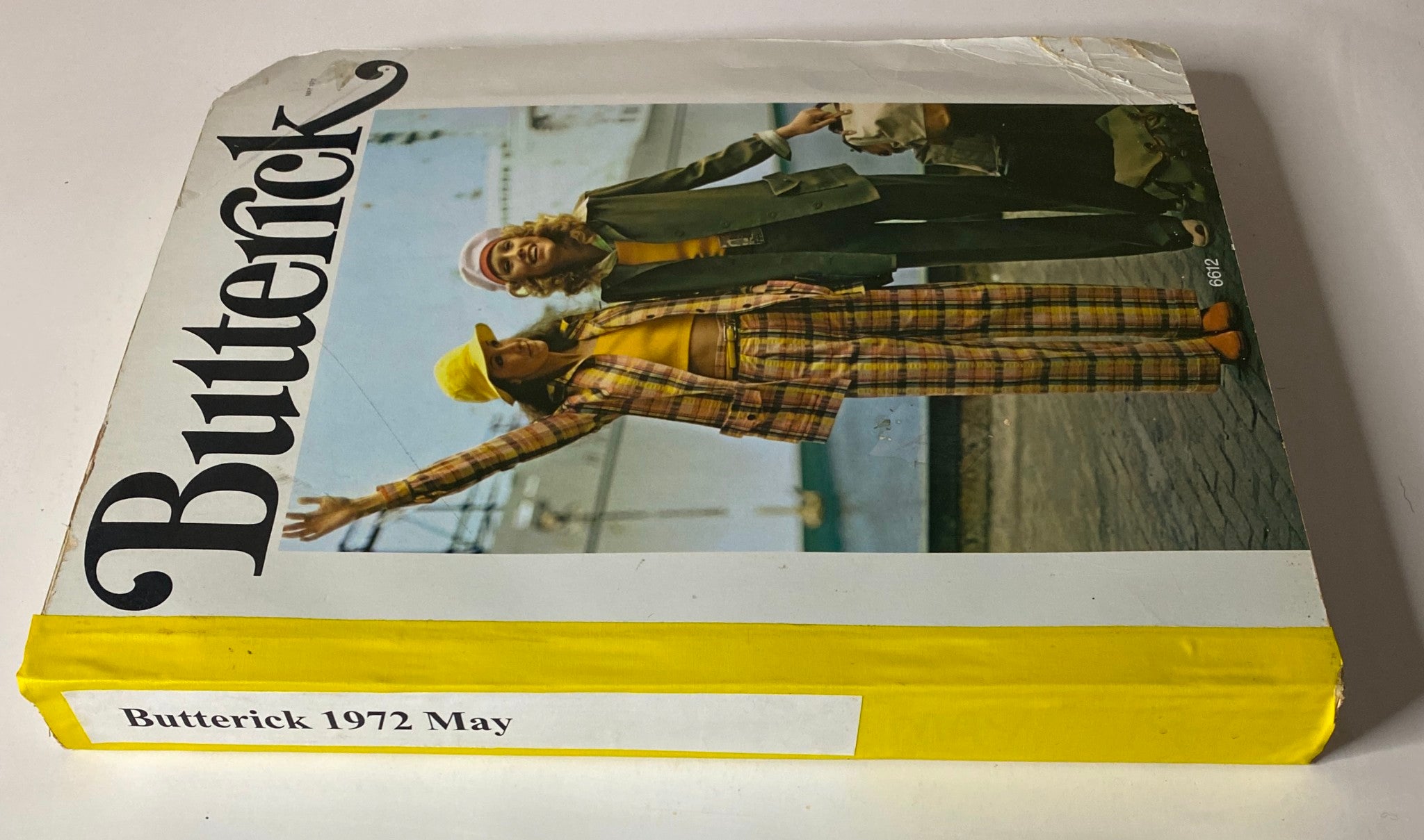 Side view of the 1972 May Butterick Catalog, highlighting its design and colorful cover with a playful representation of 1970s fashion and models in fashionable attire.