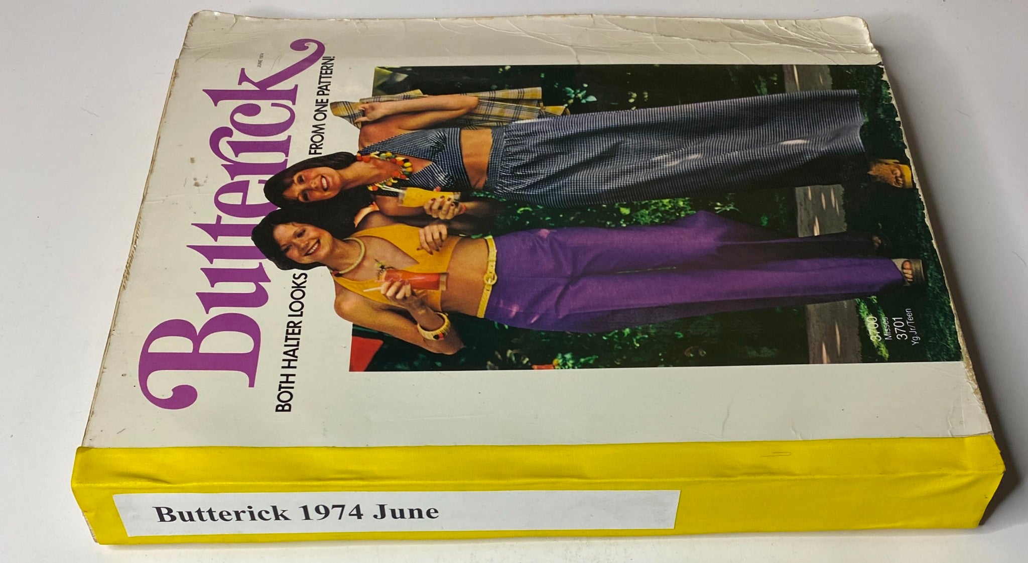 Another view of the 1974 June Butterick Catalog cover featuring two models in stylish halter top outfits, with bold typography stating 'Butterick 1974 June' and the tagline 'Both Halter Looks From One Pattern!' highlighting its collection of coordinated fashions.