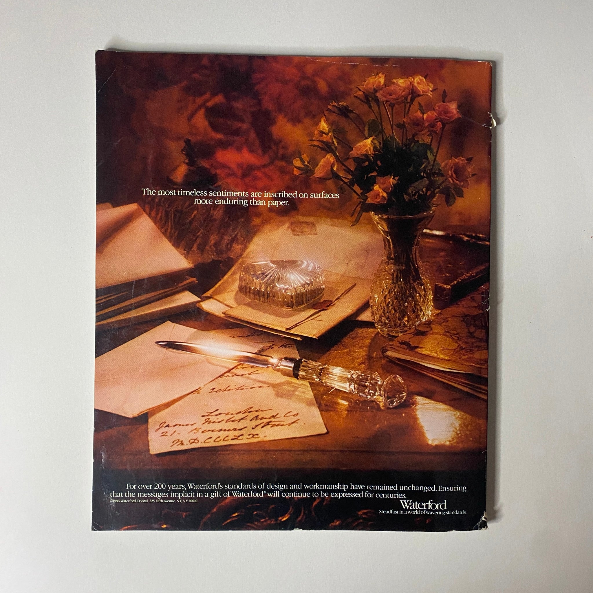 An advertisement featuring elegant stationery, a crystal inkstand, and roses that conveys the sentiment 'The most timeless sentiments are inscribed on surfaces more enduring than paper.' This image promotes Waterford, reflecting craftsmanship and elegance in writing. Connoisseur Magazine March 1987 The Unknown British Museum No Label.