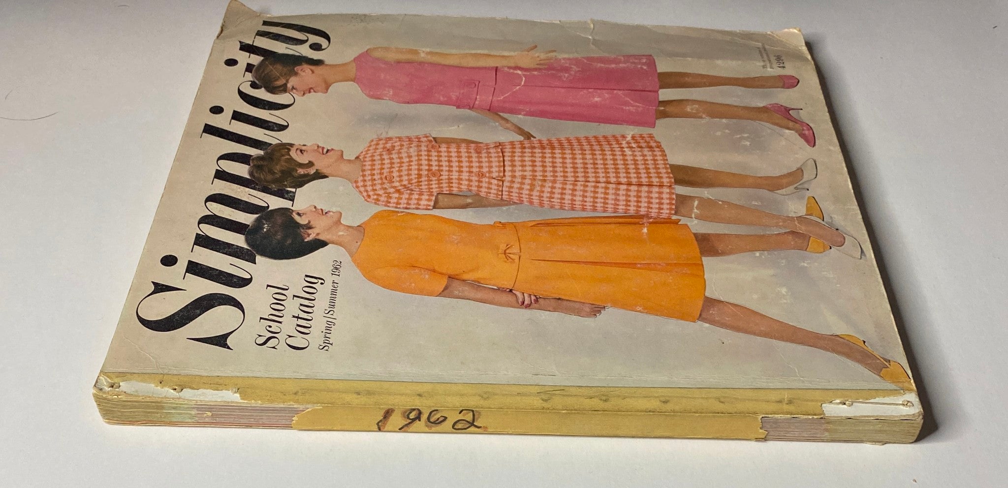 1962 Simplicity Spring Summer School Catalog featuring three fashion designs in vibrant colors: a pink dress, a gingham midi, and an orange dress on the cover.