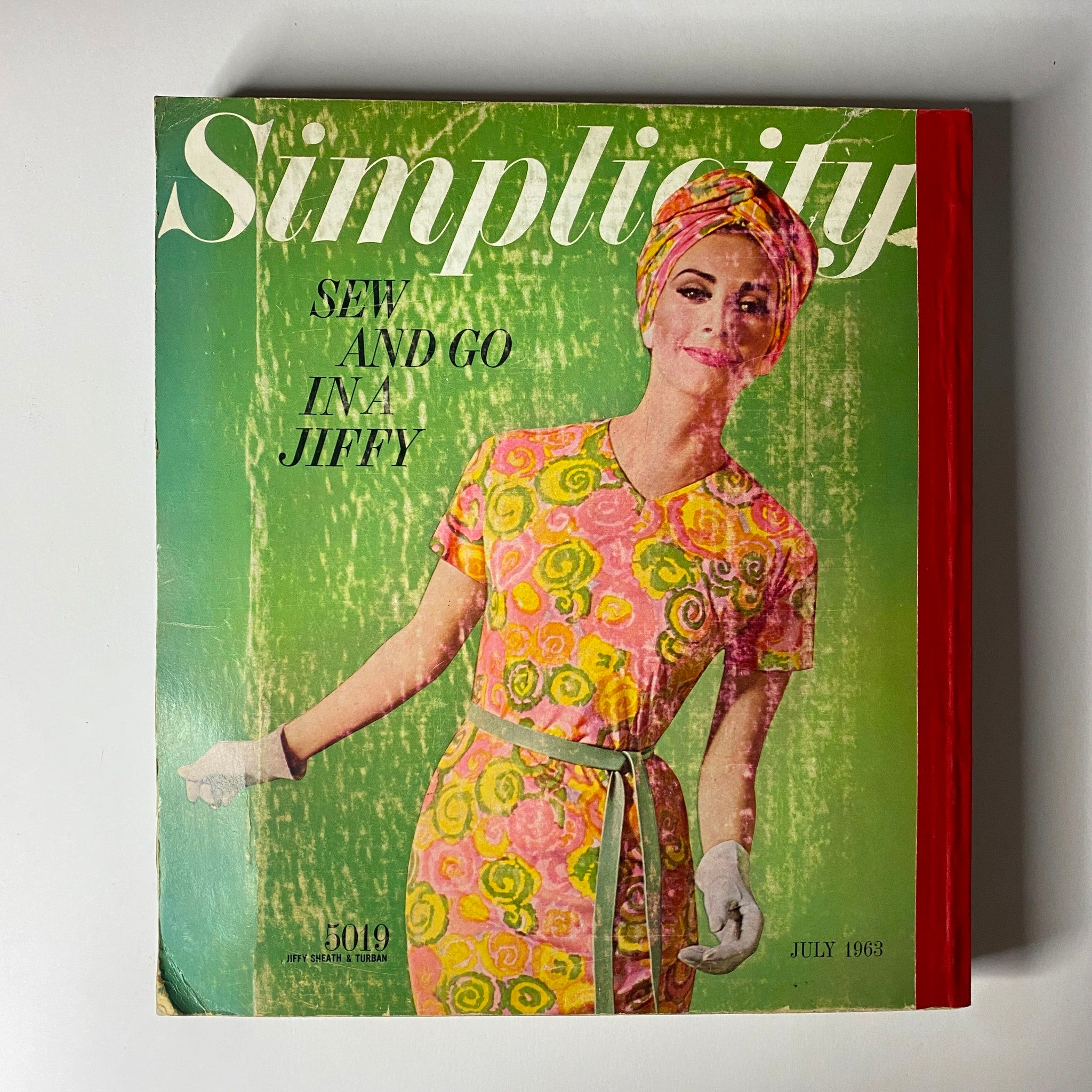 Cover of the 1963 July Simplicity Sew Catalog showcasing vibrant fashion patterns for home sewing. The cover features a smiling woman in a floral dress with a matching turban, promoting easy sewing patterns in a stylish design.