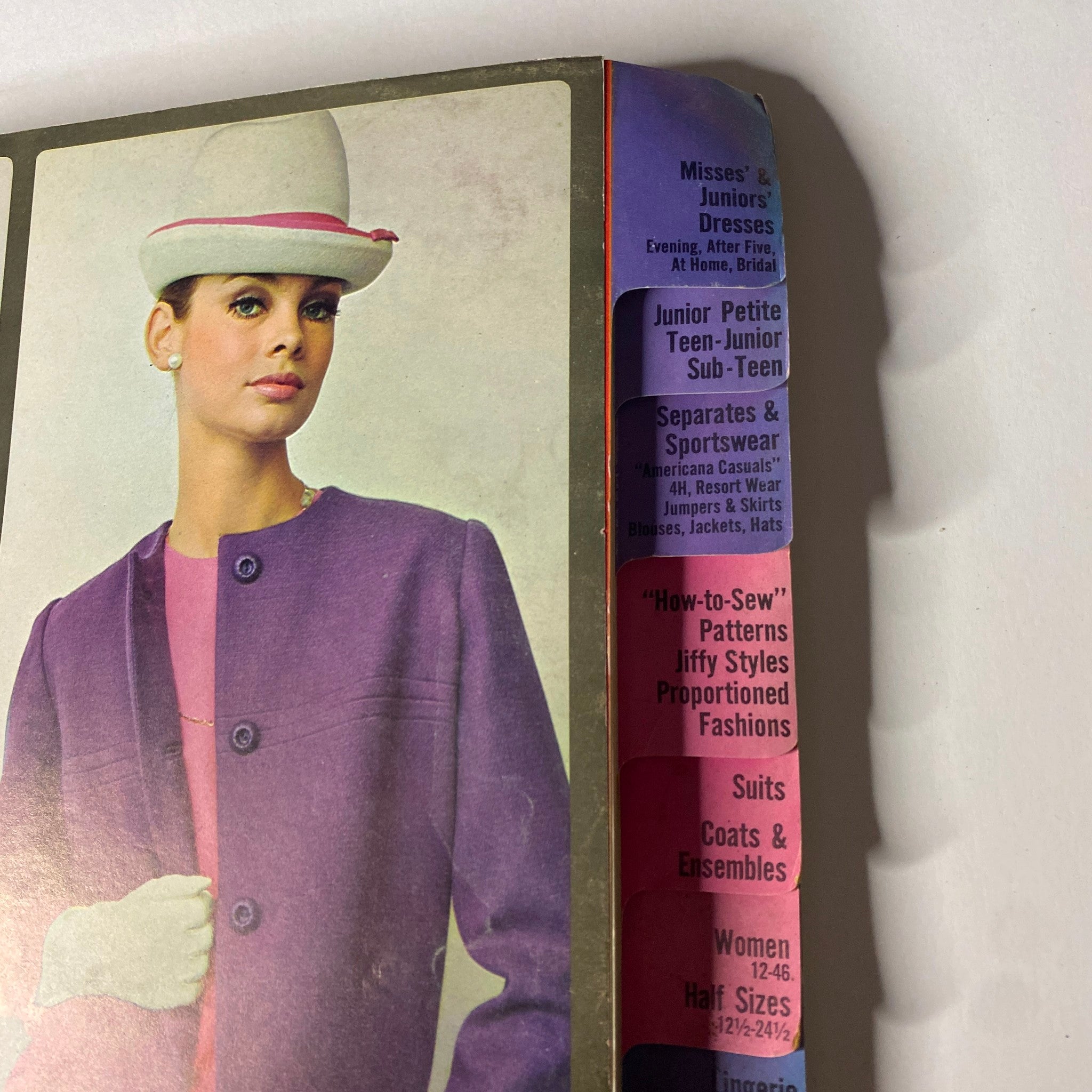 Close-up of the 1964 October Simplicity Fall Catalog displaying women's fashion patterns, including a stylish model in a purple coat and matching hat.