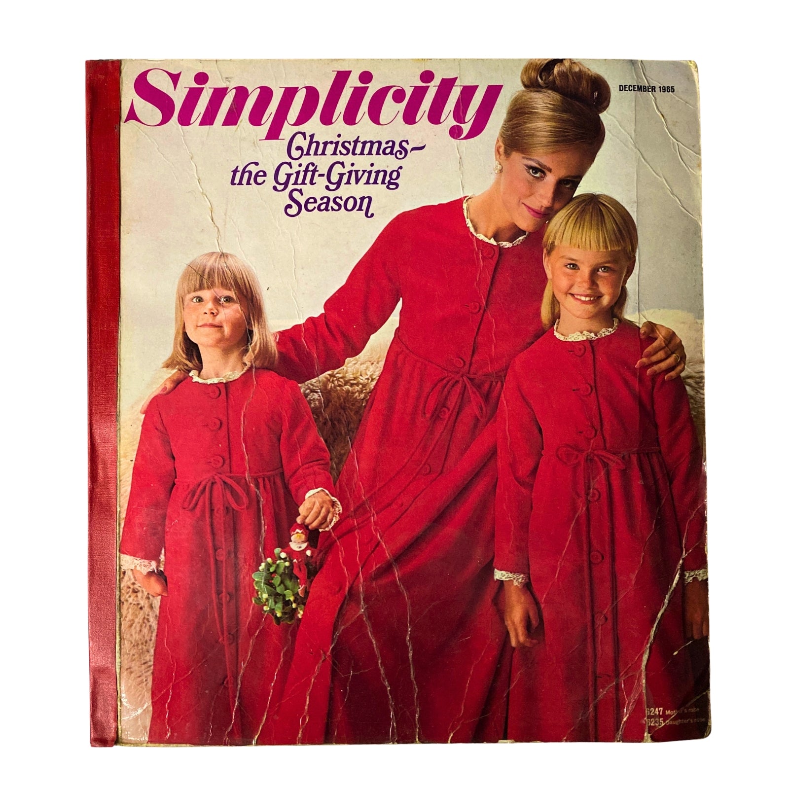 Cover of the 1965 December Simplicity Christmas Catalog showcasing holiday sewing patterns, featuring a woman and two girls in matching red dresses holding a decorative wreath.