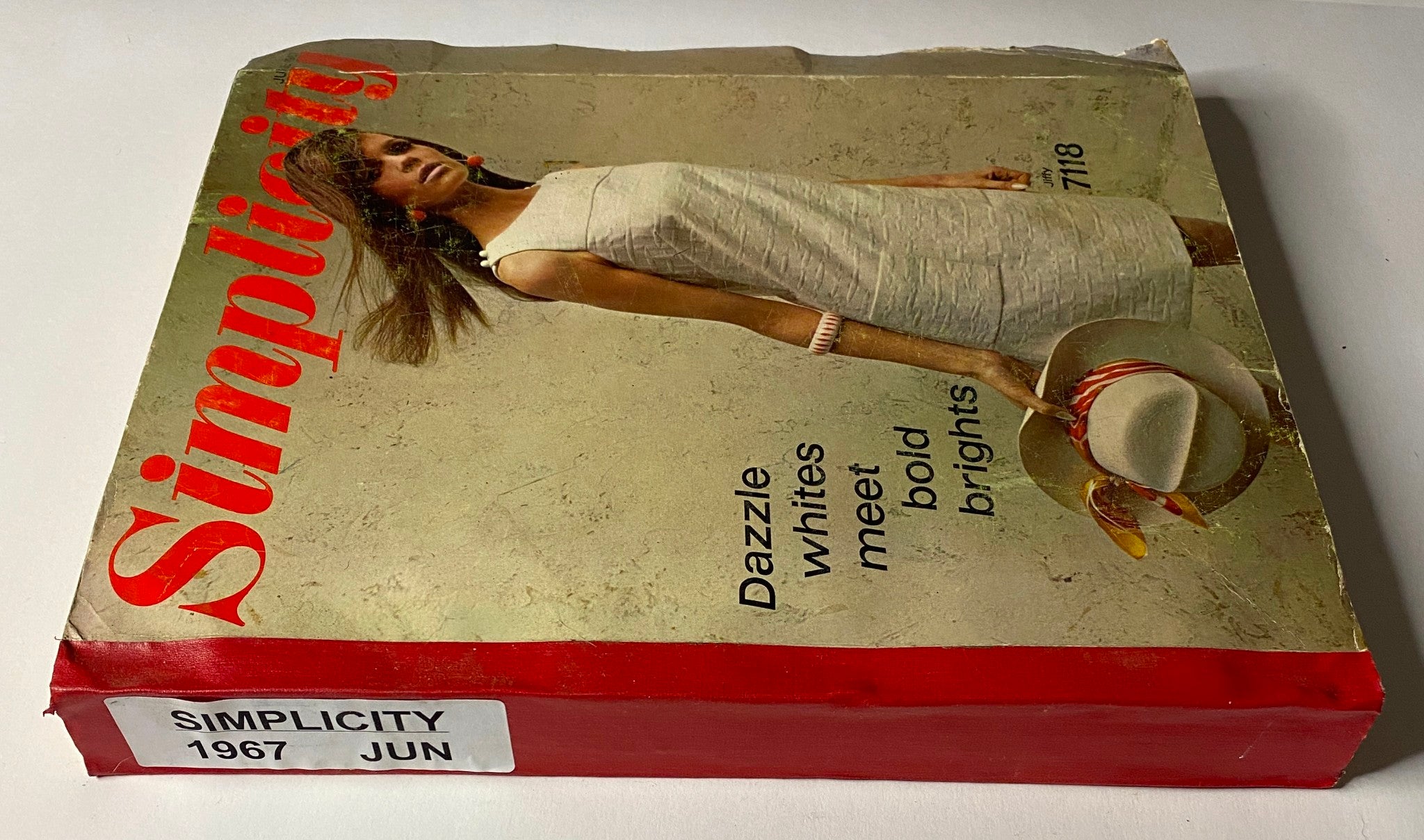 Side view of the 1967 June Simplicity Sewing Pattern Catalog displaying the iconic cover design with a model in a white dress, emphasizing modern fashion styles from the late 1960s.