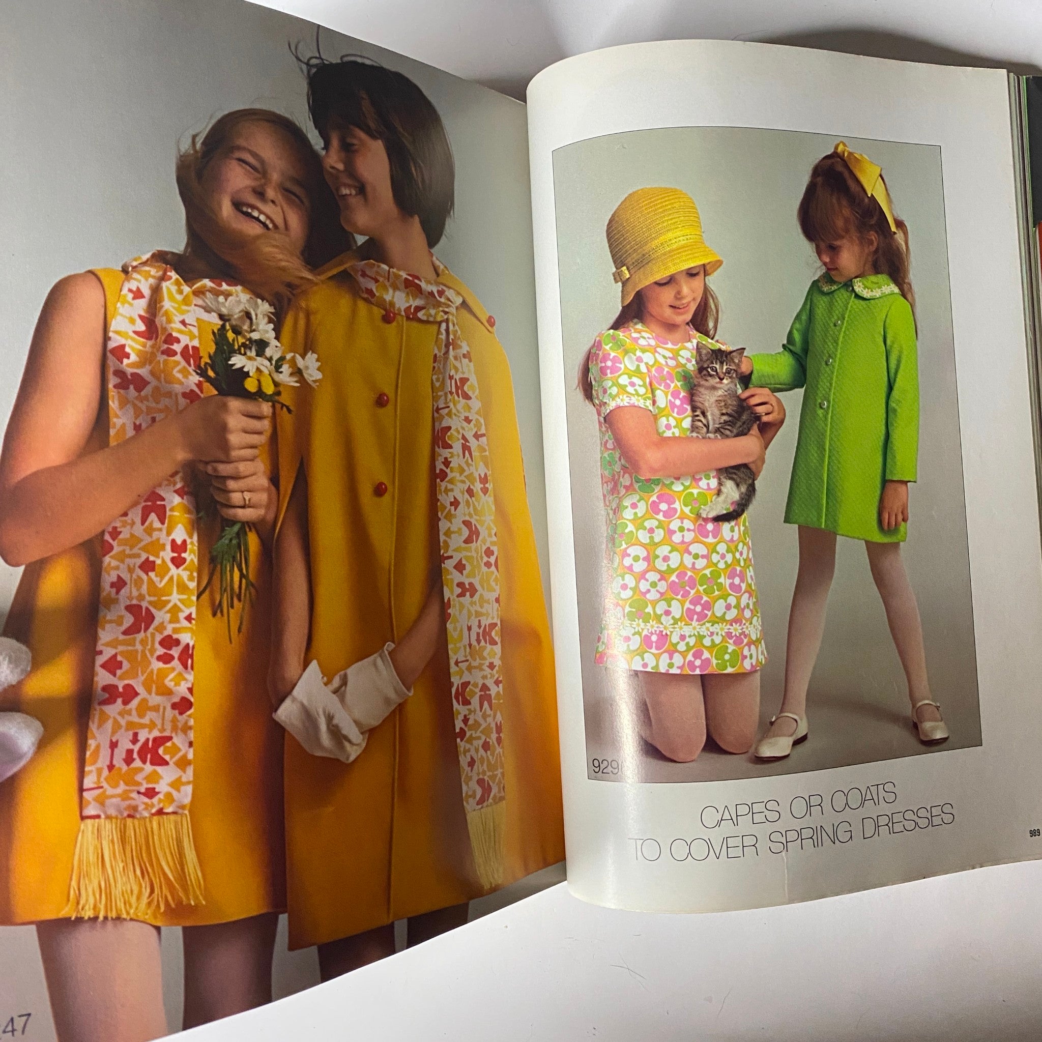 1971 April Simplicity Spring Catalog showcasing young girls in vibrant spring outfits, with one holding flowers and another cuddling a cat, highlighting the playful fashion energy of the early 1970s.