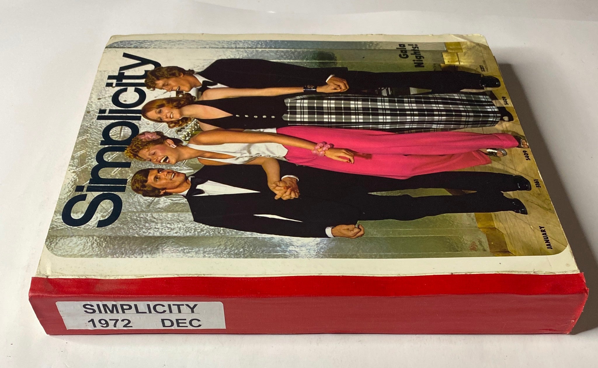 Side view of the 1972 December Simplicity Catalog highlighting stylish fashion designs for Gala Nights, with markings on the spine and colorful attire displayed.