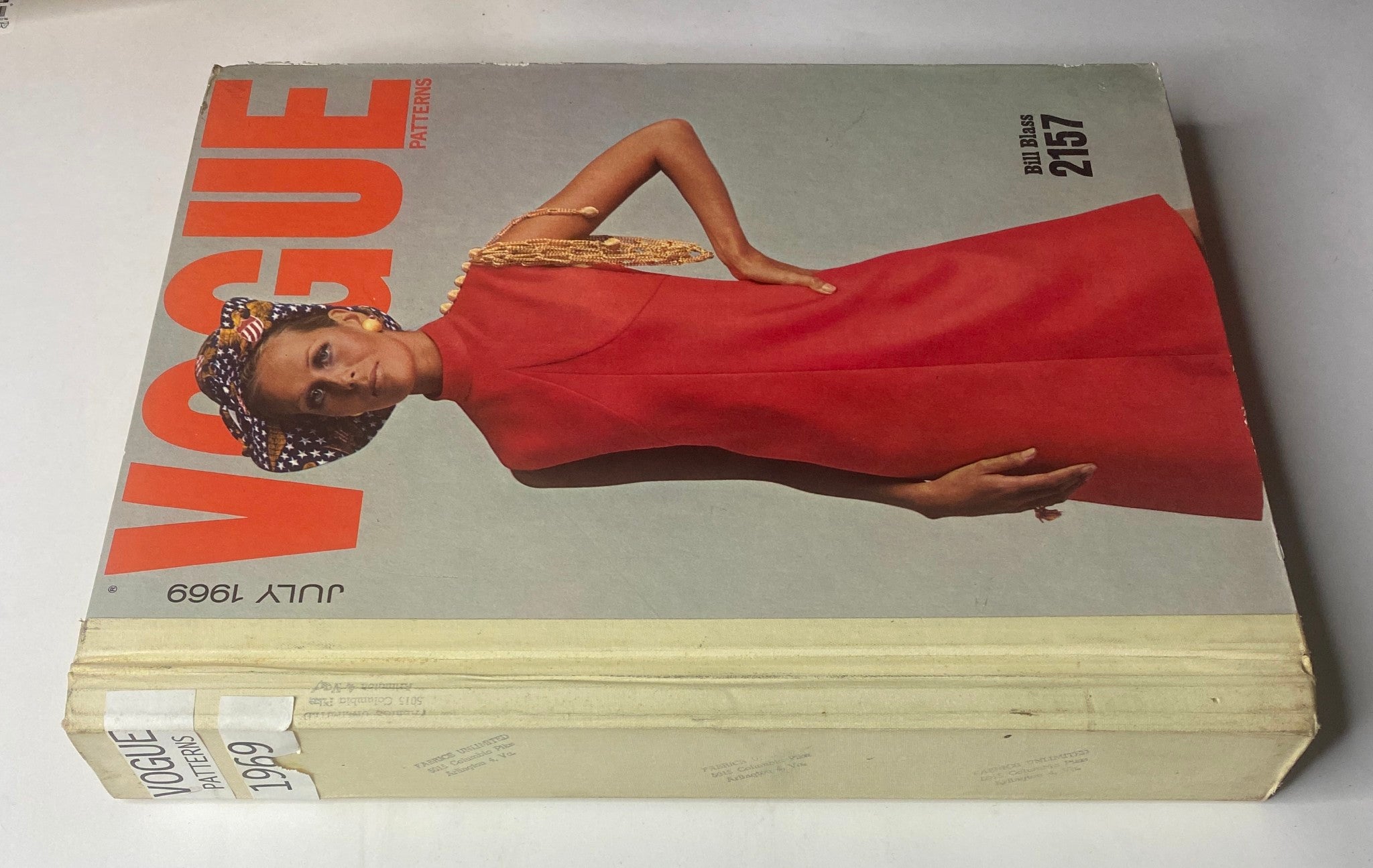 1969 Vogue Patterns July Catalog Large Store Counter Pattern Book displaying the cover of the magazine with a model in a red dress and decorative hat. Highlights vintage fashion trends from the 1960s.