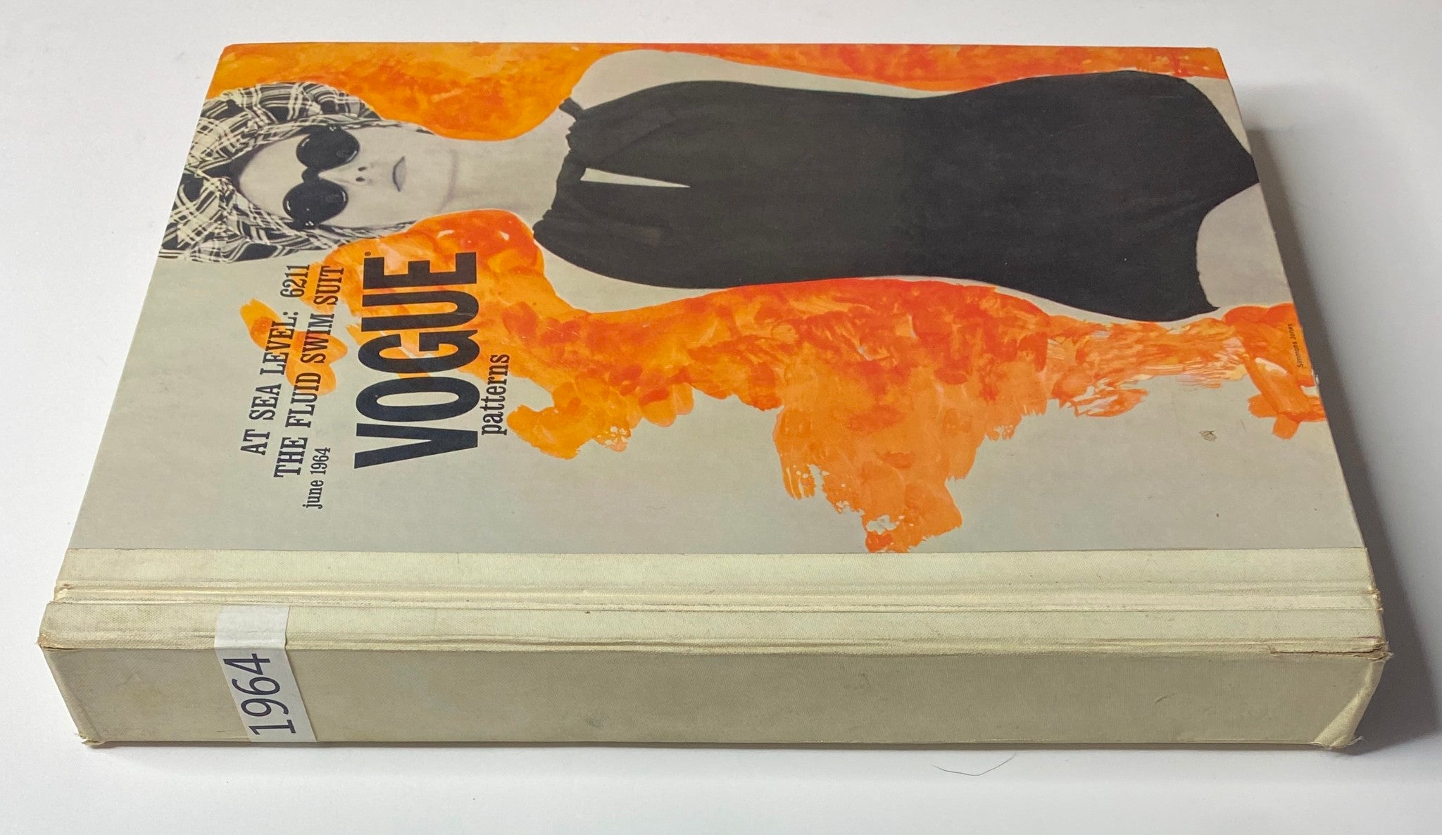 Side view of the Vogue Patterns June 1964 Catalog cover, displaying a stylish model in a black swimsuit against a vibrant orange background.