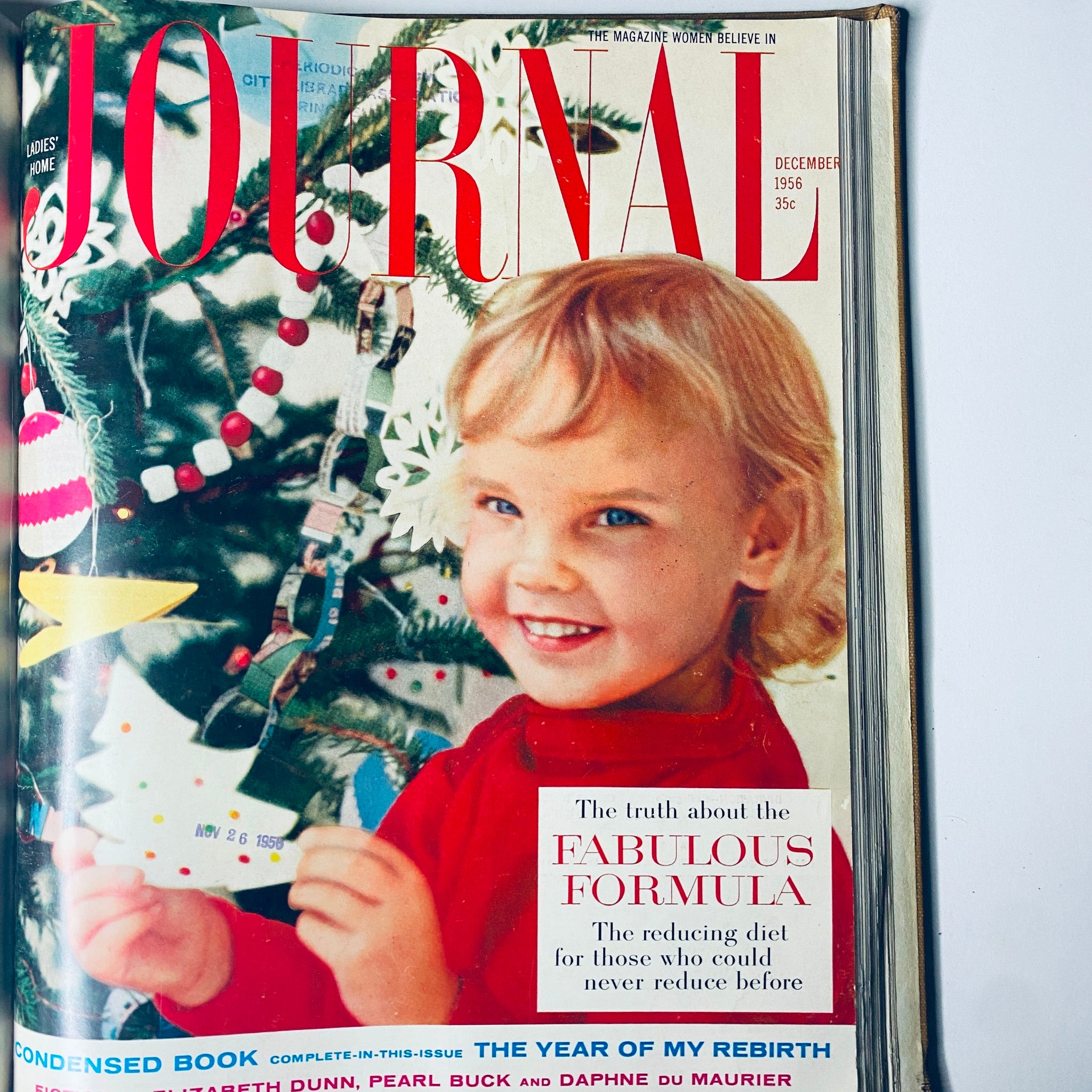Cover of Ladies' Home Journal December 1956 depicting a cheerful young girl in front of a Christmas tree, highlighting family and holiday themes of the era.