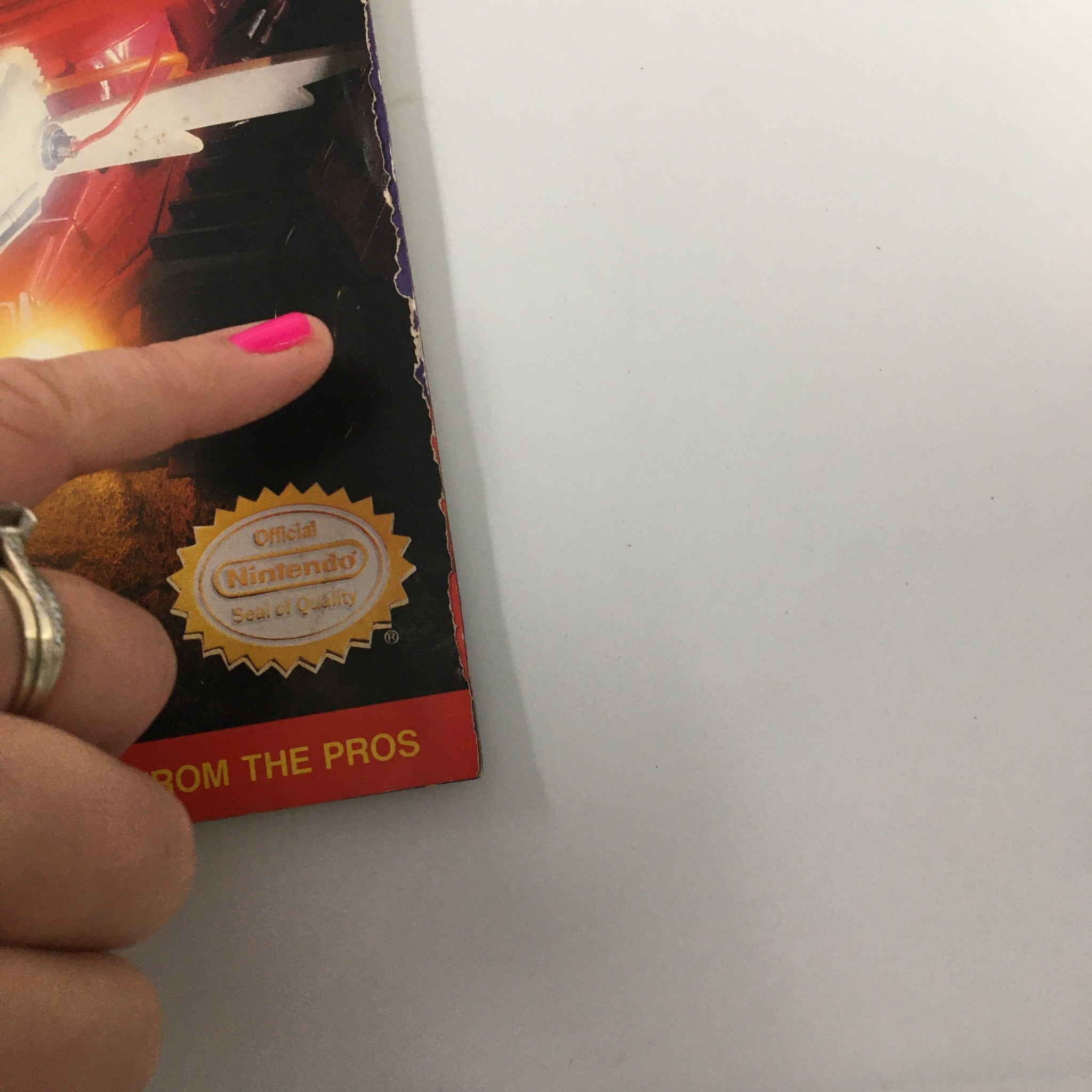 Detail shot of the bottom corner of Nintendo Power Magazine August 1991, Issue #27, highlighting the Official Nintendo Seal of Quality with a finger pointing at it.