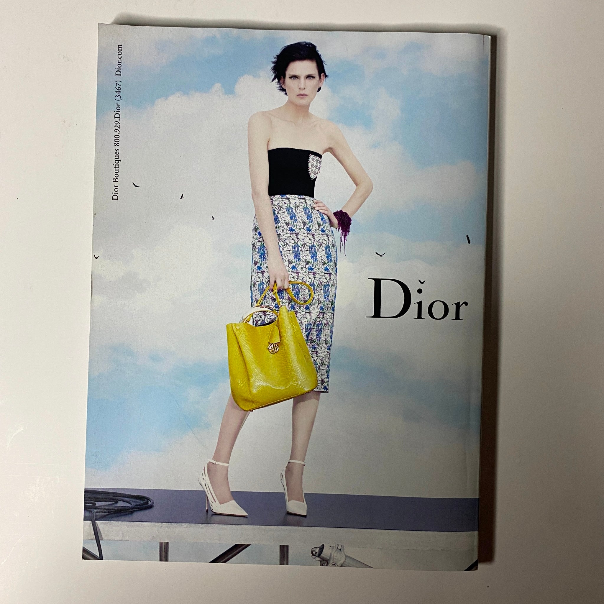 A fashion advertisement in Vogue Magazine February 2014 featuring Dior, showcasing a model in a chic outfit holding a bright yellow handbag, embodying contemporary elegance.