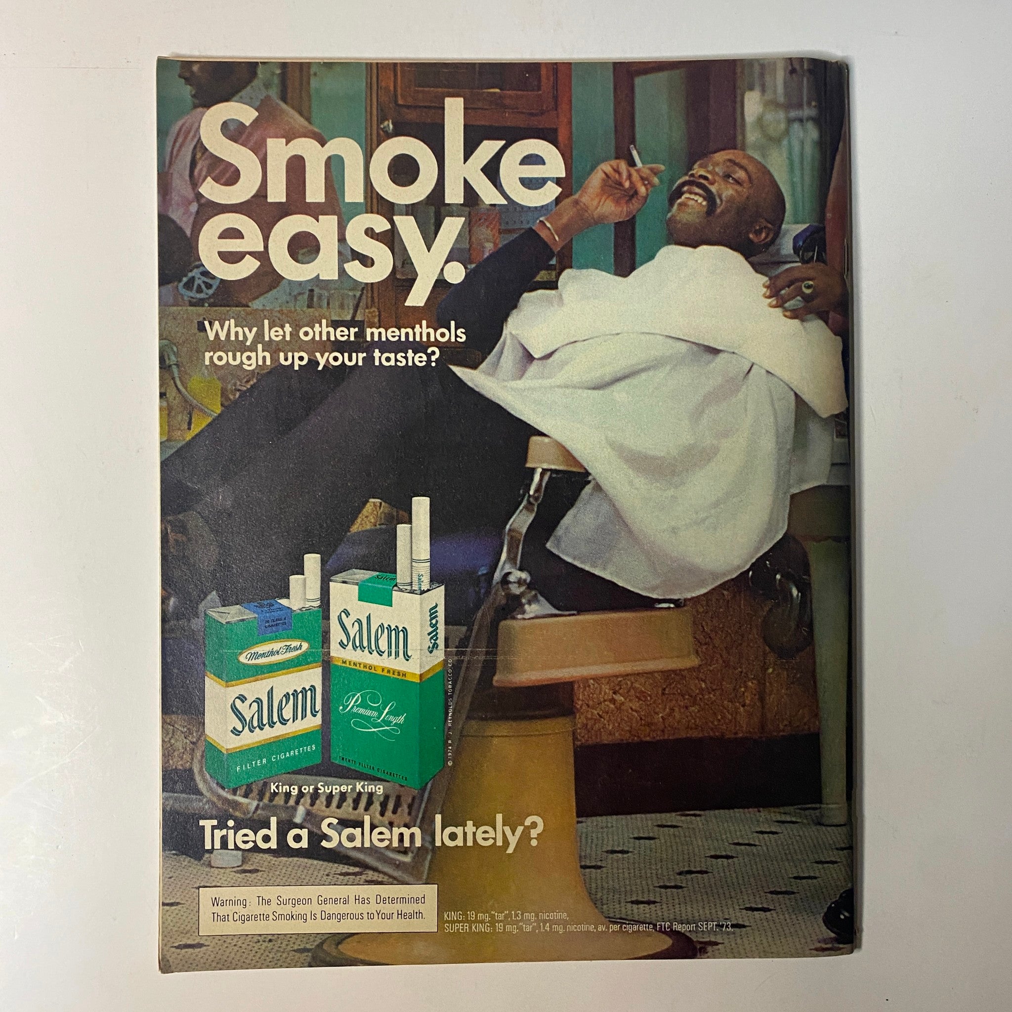 Vintage advertisement from Black Sports Magazine July 1974 featuring a man getting a haircut while enjoying a cigarette, promoting Salem menthol cigarettes. Ad highlights the slogan 'Smoke easy. Why let other menthols rough up your taste?' in the context of 1970s culture.