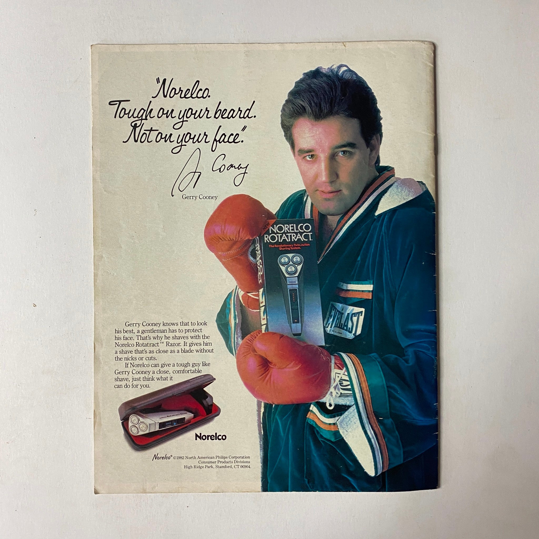 Gerry Cooney promoting Norelco shavers in an advertisement, wearing boxing gloves and a robe, emphasizing the slogan 'Tough on your beard. Not on your face.' from the 1982 Caesar's Palace boxing event program.