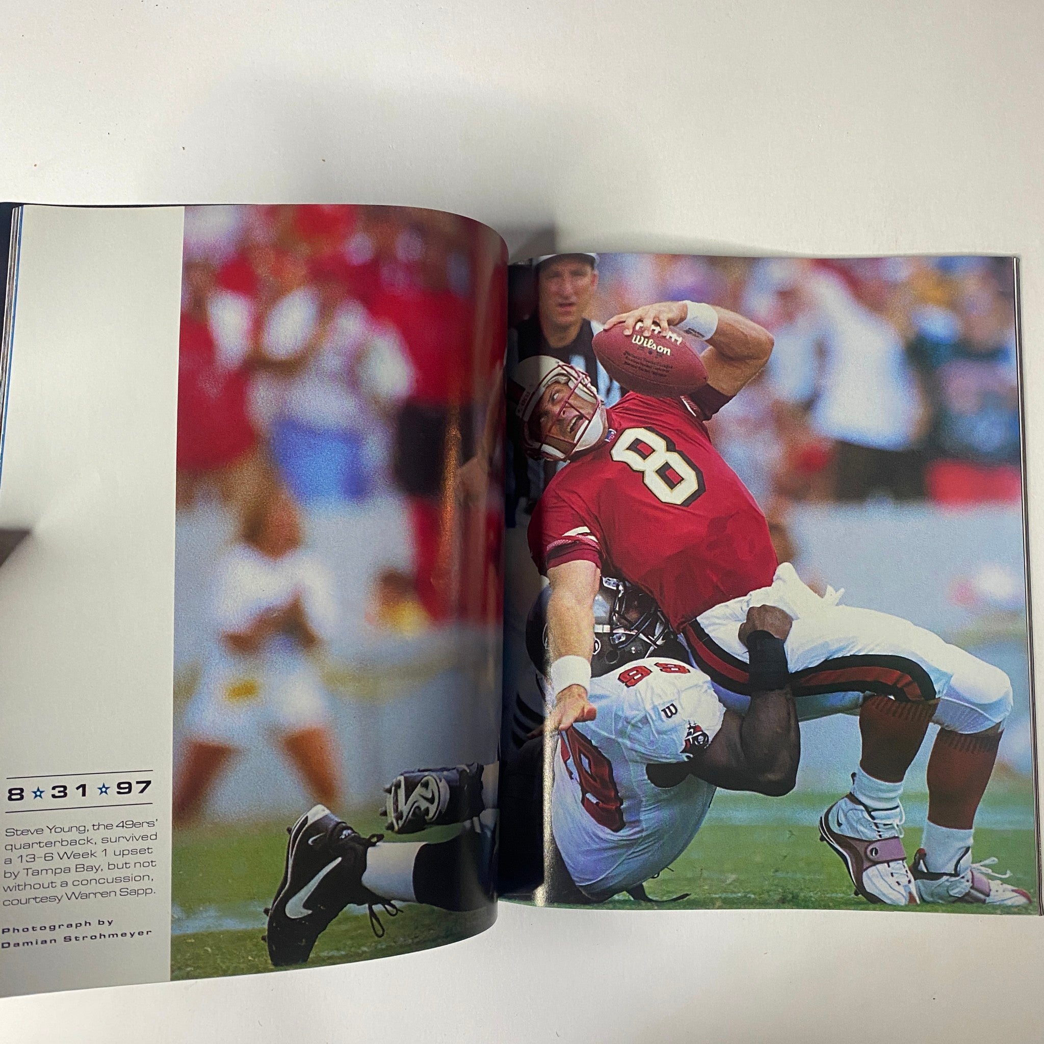 Sports Illustrated Magazine - Tiger Woods YEAR IN PICTURES 1997 features a dynamic image of football player Steve Young executing a pass while being tackled during a game.