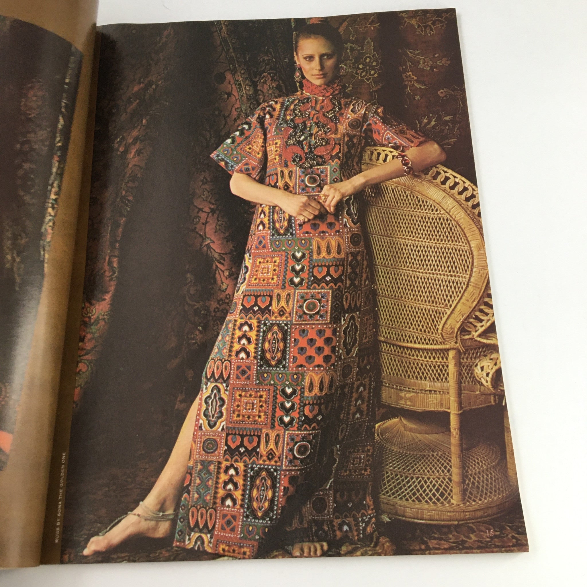 Fashion model in a striking patterned maxi dress, posed elegantly by a wicker chair, emphasizing 1970s style from the International Vogue Pattern Book June 1970 New Shapes for Sun Country.