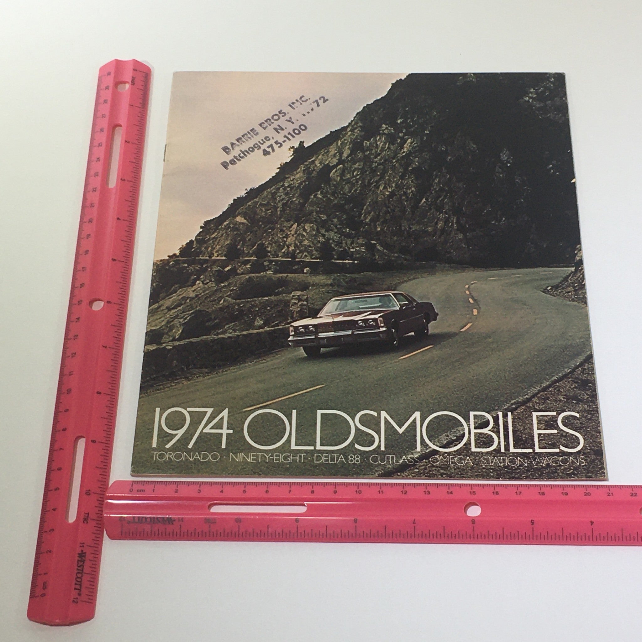 Front cover of the Vintage 1974 Oldsmobile Toronado NinetyEight Station Wagons Car Catalog Brochure showcasing a classic car in a scenic setting with measurements for display.